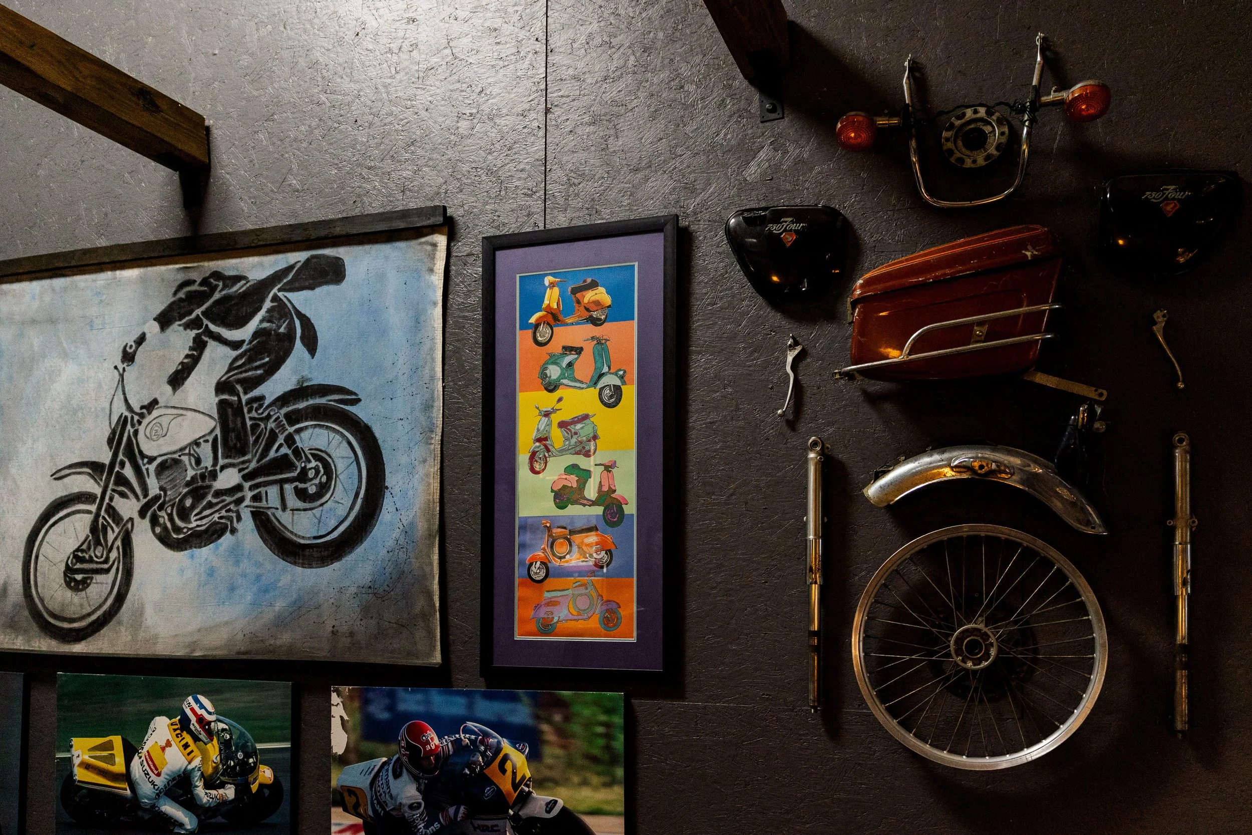 A wall decorated with vintage motorcycle, scooter, and racing posters, along with various motorcycle parts and accessories. Vintage motorcycle collection on display at Birmingham Vintage Cycle in Birmingham Alabama
