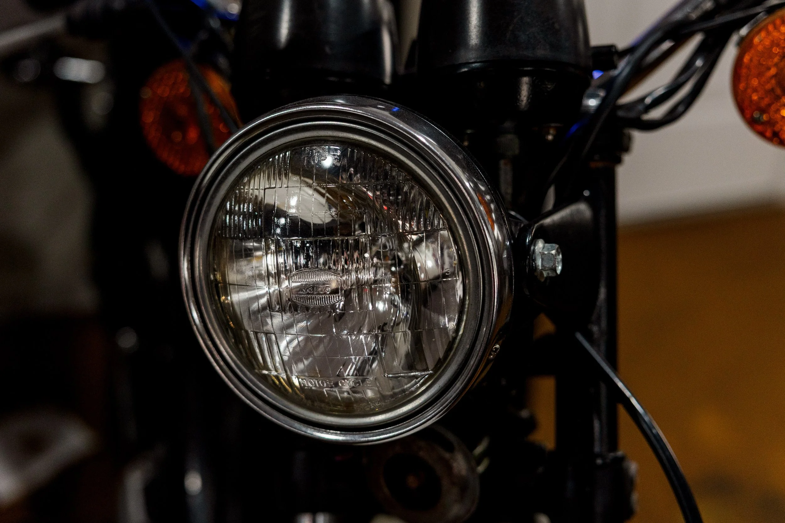 Front view of a motorcycle headlight with surrounding black frame and orange turn signals on each side. Vintage motorcycle detail at Birmingham Vintage Cycle, a vintage motorcycle restoration shop in Birmingham Alabama