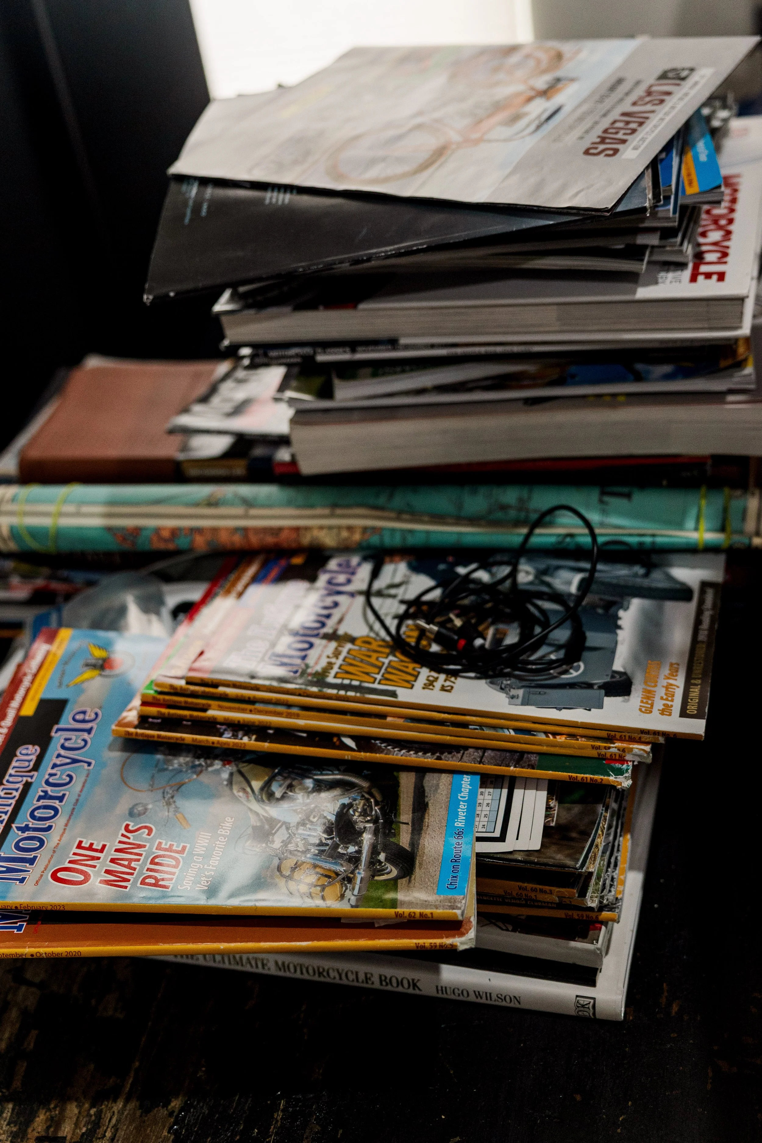 Stack of motorcycle and travel magazines on a table, with a pair of in-ear headphones on top. Inside Birmingham Vintage Cycle, a vintage motorcycle shop and community space in Birmingham Alabama