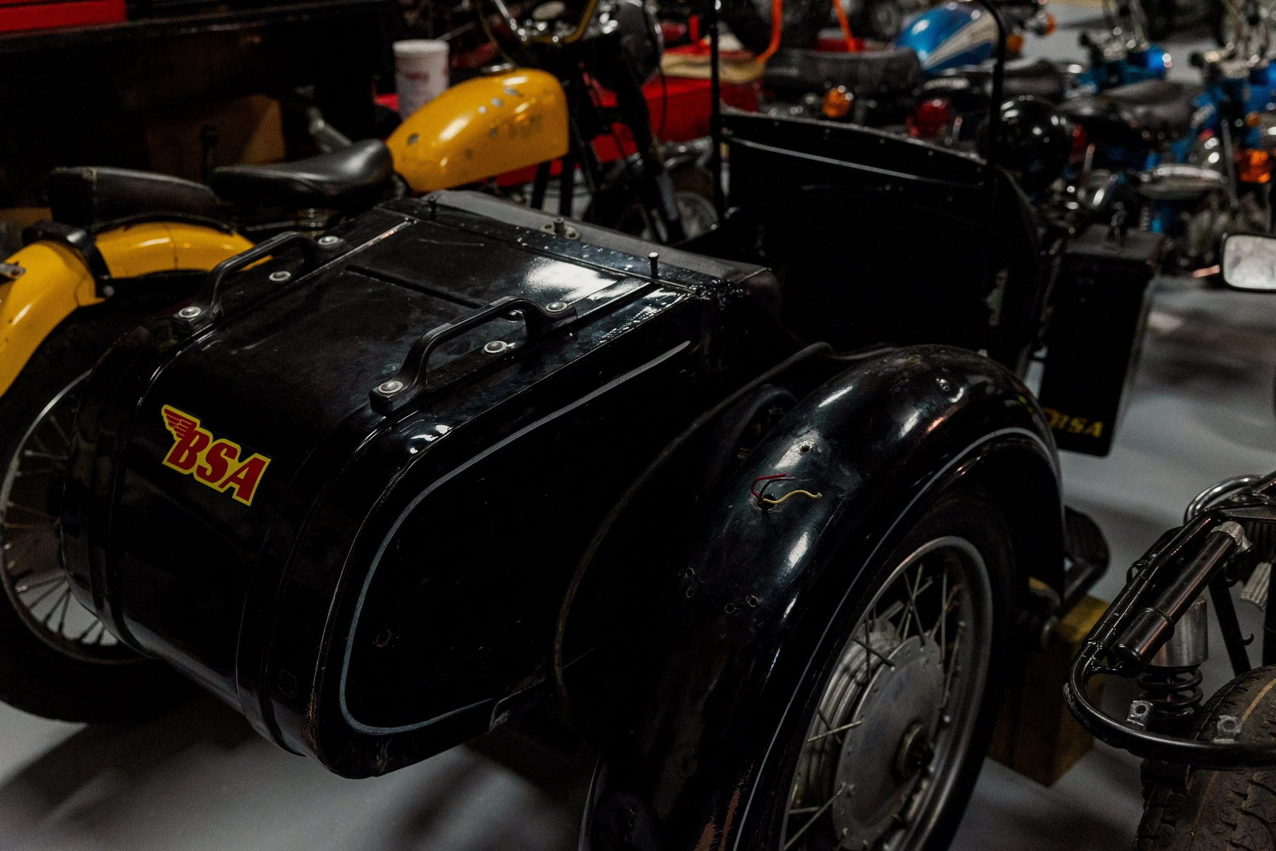 Several vintage motorcycles and sidecars are parked closely together in a dimly lit space, with some showing visible signs of wear. Vintage motorcycle collection on display at Birmingham Vintage Cycle in Birmingham Alabama