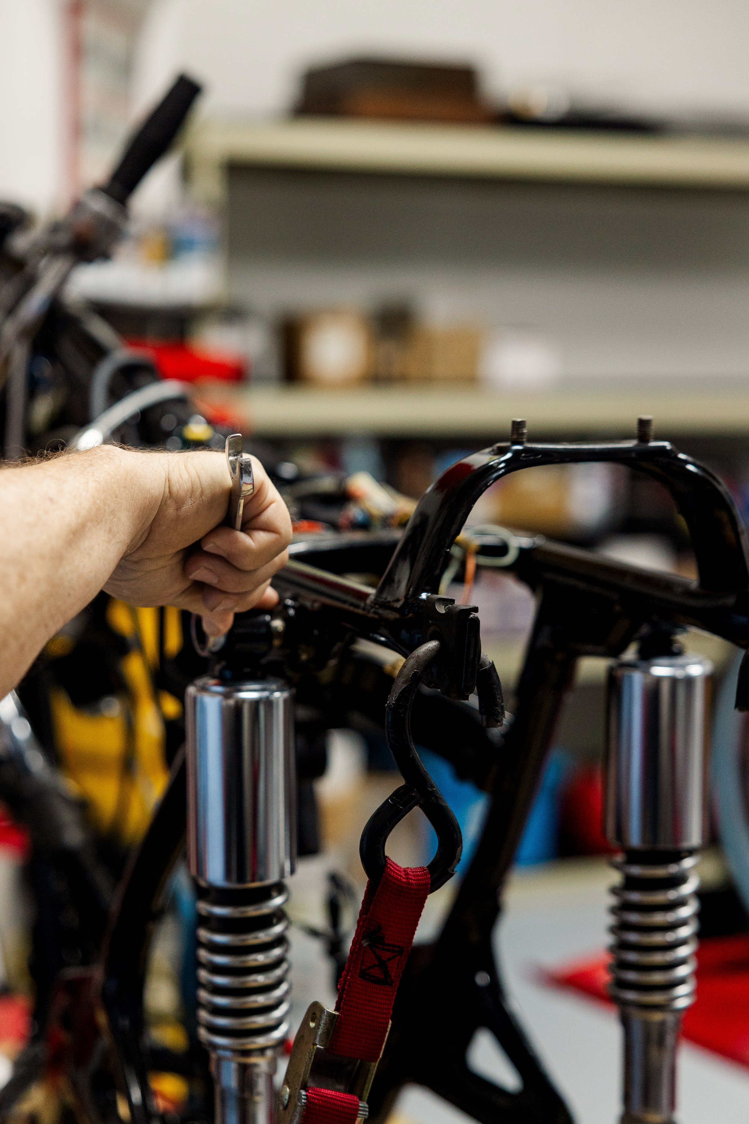 Close-up of a person using a wrench to work on a motorcycle frame in a workshop, with tools and shelves in the background. Vintage motorcycle detail at Birmingham Vintage Cycle, a vintage motorcycle restoration shop in Birmingham Alabama