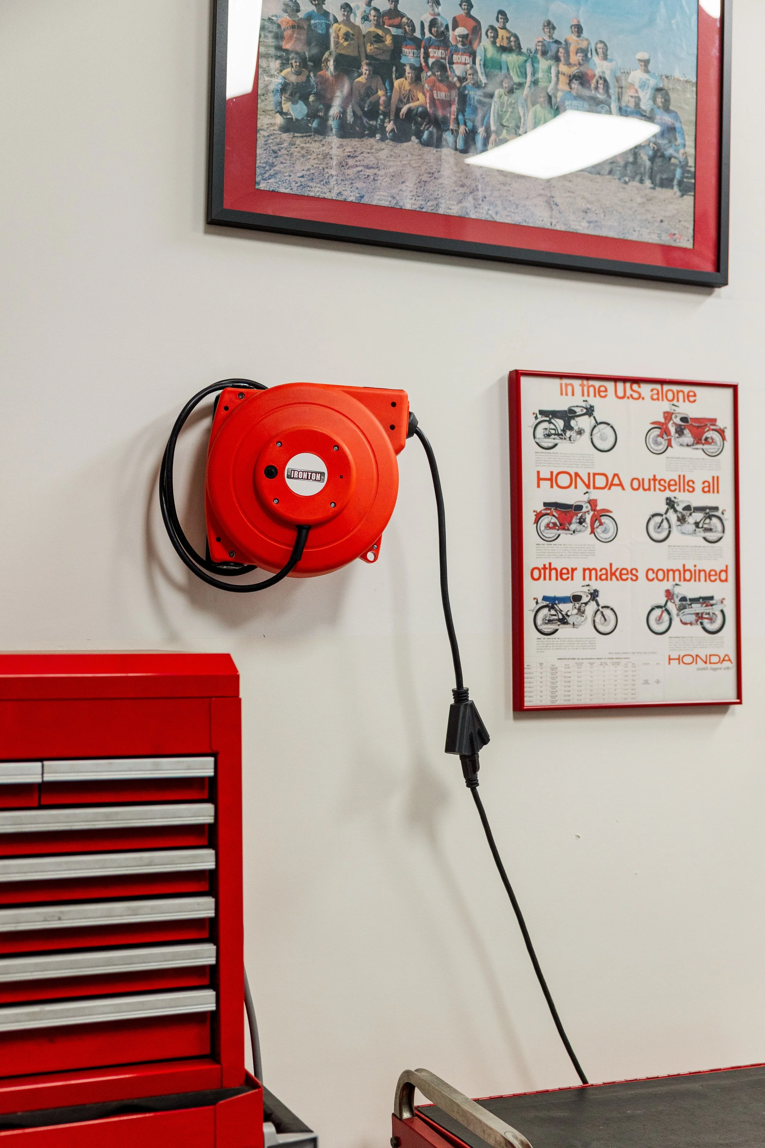 Red toolbox and red fire alarm on a white wall, with a vintage motorcycle poster and a motorcycle diagram beside them. Inside Birmingham Vintage Cycle, a vintage motorcycle shop and community space in Birmingham Alabama