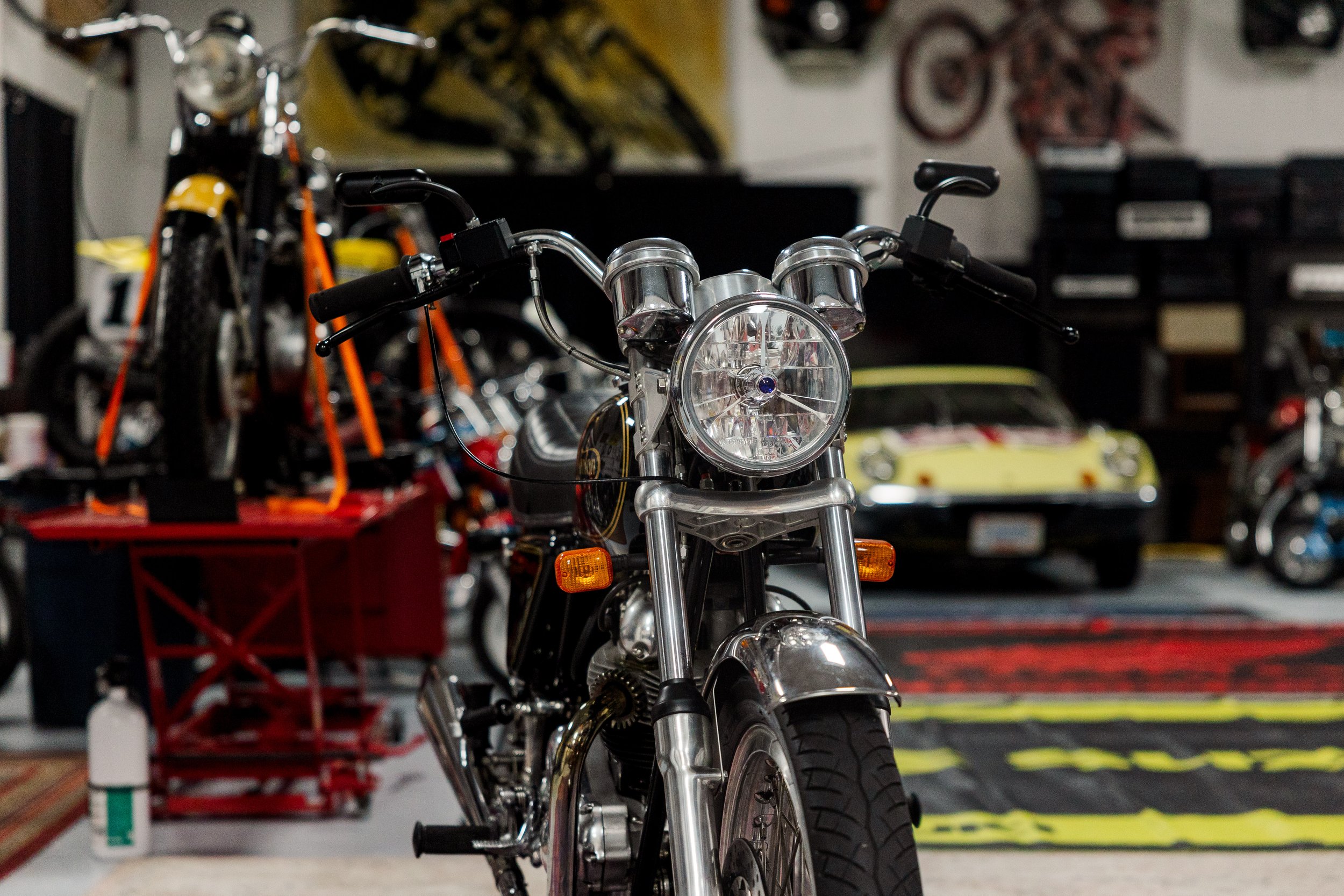 A motorcycle parked indoors with other bikes and automotive supplies in the background. Vintage motorcycle detail at Birmingham Vintage Cycle, a vintage motorcycle restoration shop in Birmingham Alabama