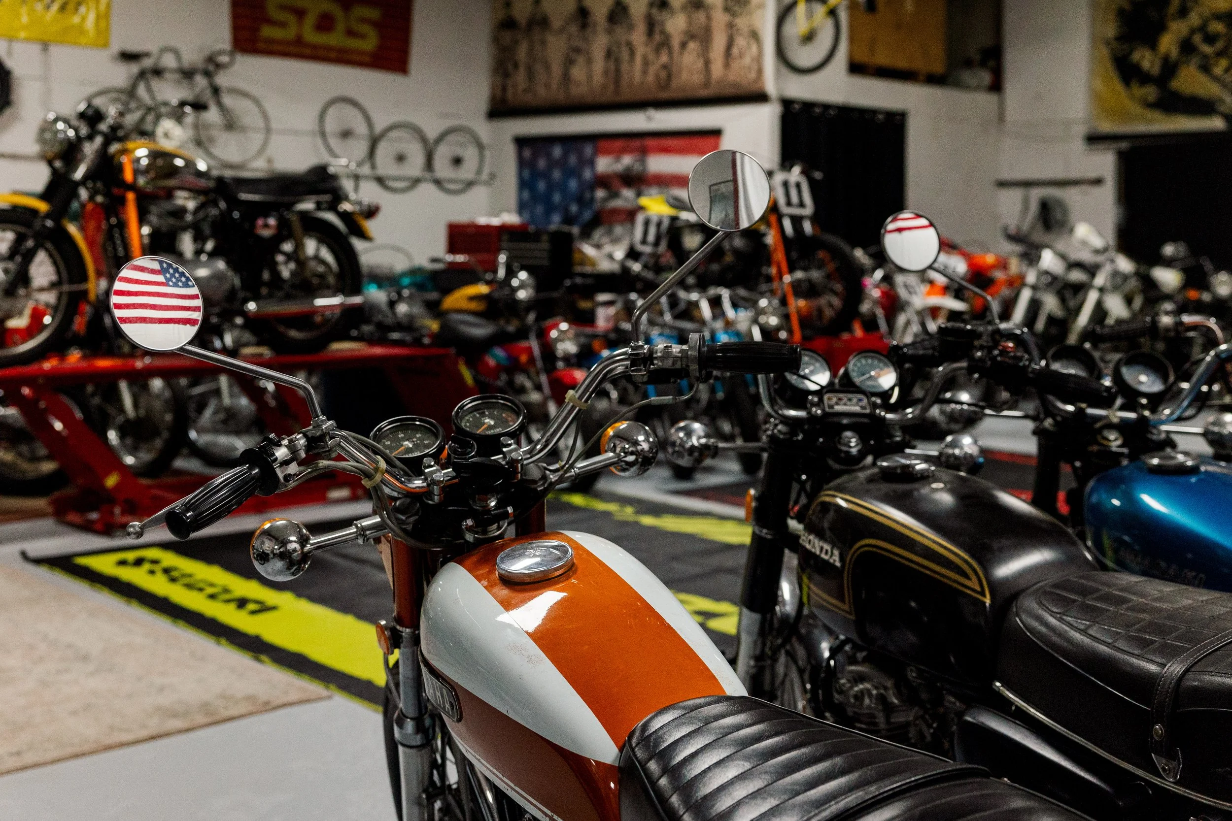 Various vintage motorcycles and bikes in a garage or showroom with American flags and posters on the walls. Vintage motorcycle collection on display at Birmingham Vintage Cycle in Birmingham Alabama