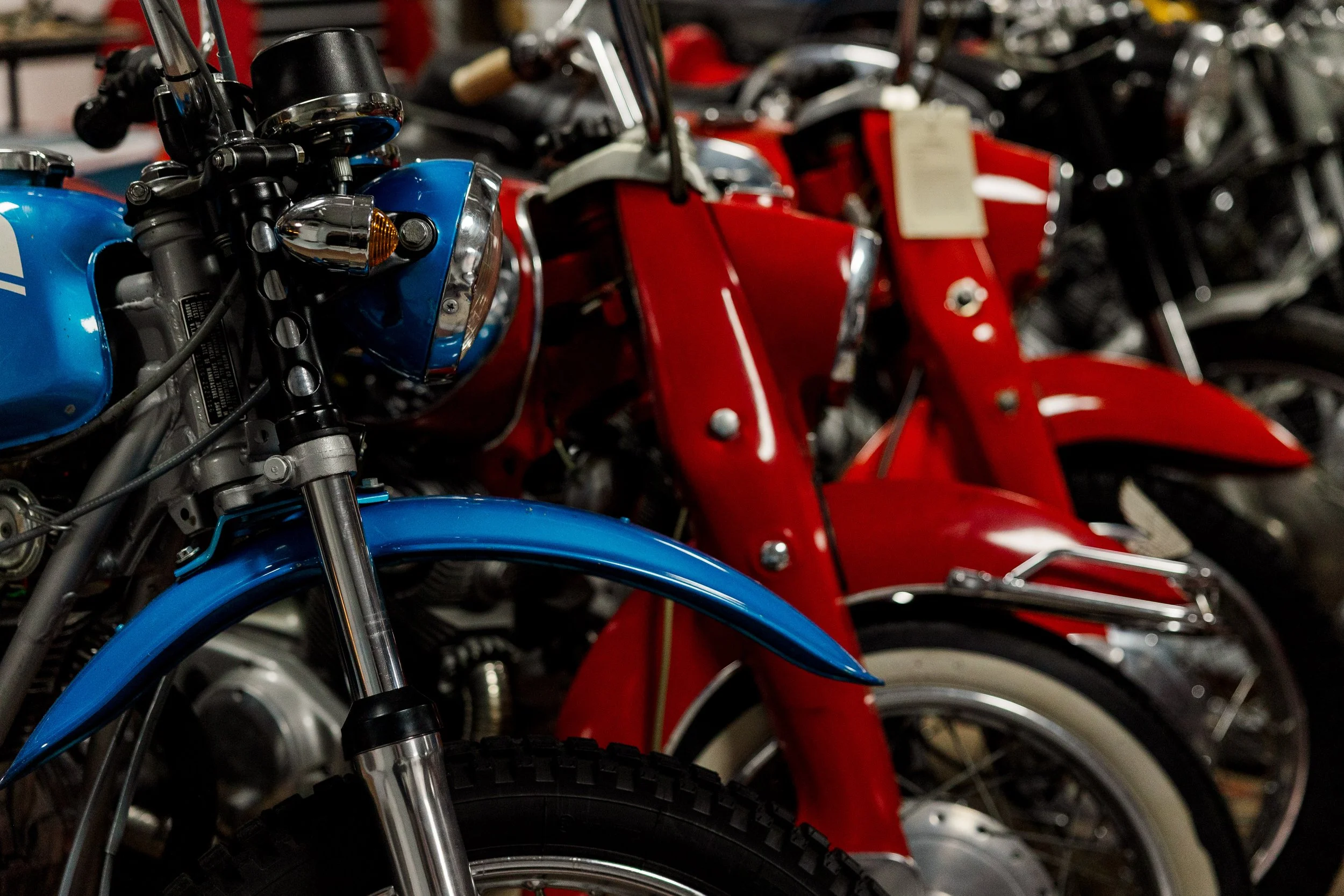 Lineup of vintage motorcycles in a museum, highlighting the front parts with blue and red paint. Vintage motorcycle collection on display at Birmingham Vintage Cycle in Birmingham Alabama