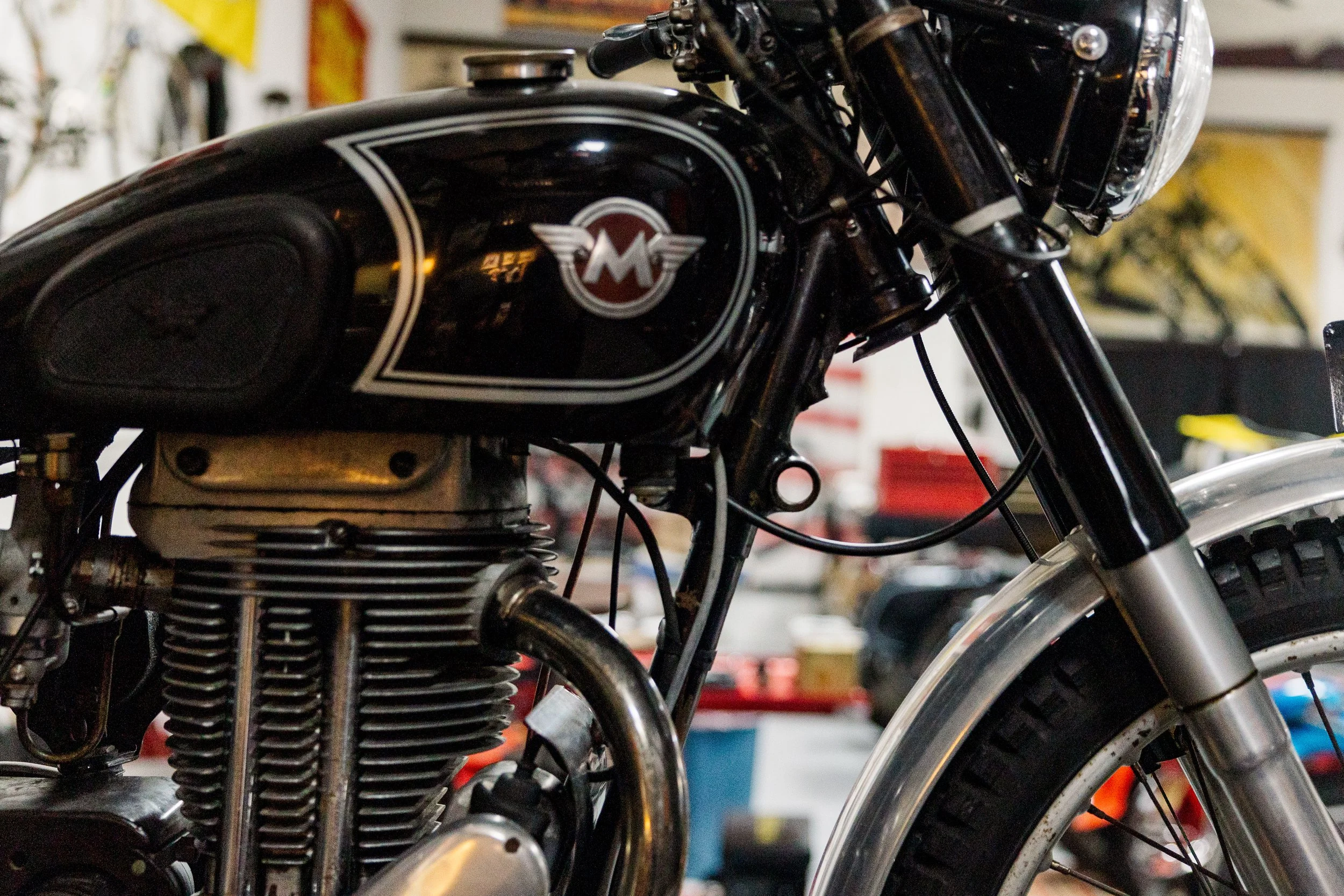 Close-up of a vintage black motorcycle with a Harley-Davidson logo on the fuel tank, showing parts of the engine, front wheel, and handlebars. Vintage motorcycle detail at Birmingham Vintage Cycle, a vintage motorcycle restoration shop in Birmingham 