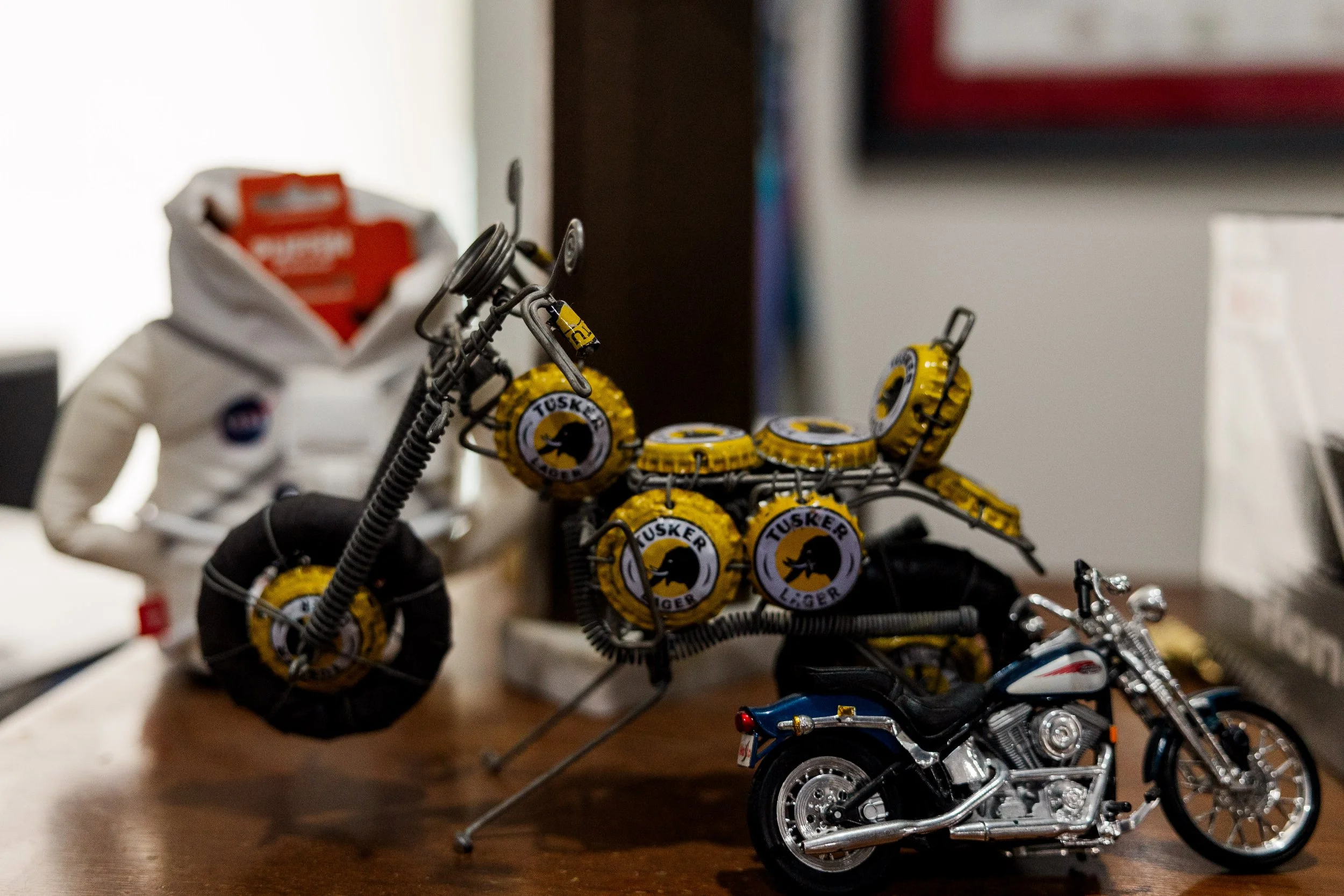Close-up of toy motorcycles and a toy dirt bike, with a background of blurred objects, including some white and red items. Inside Birmingham Vintage Cycle, a vintage motorcycle shop and community space in Birmingham Alabama