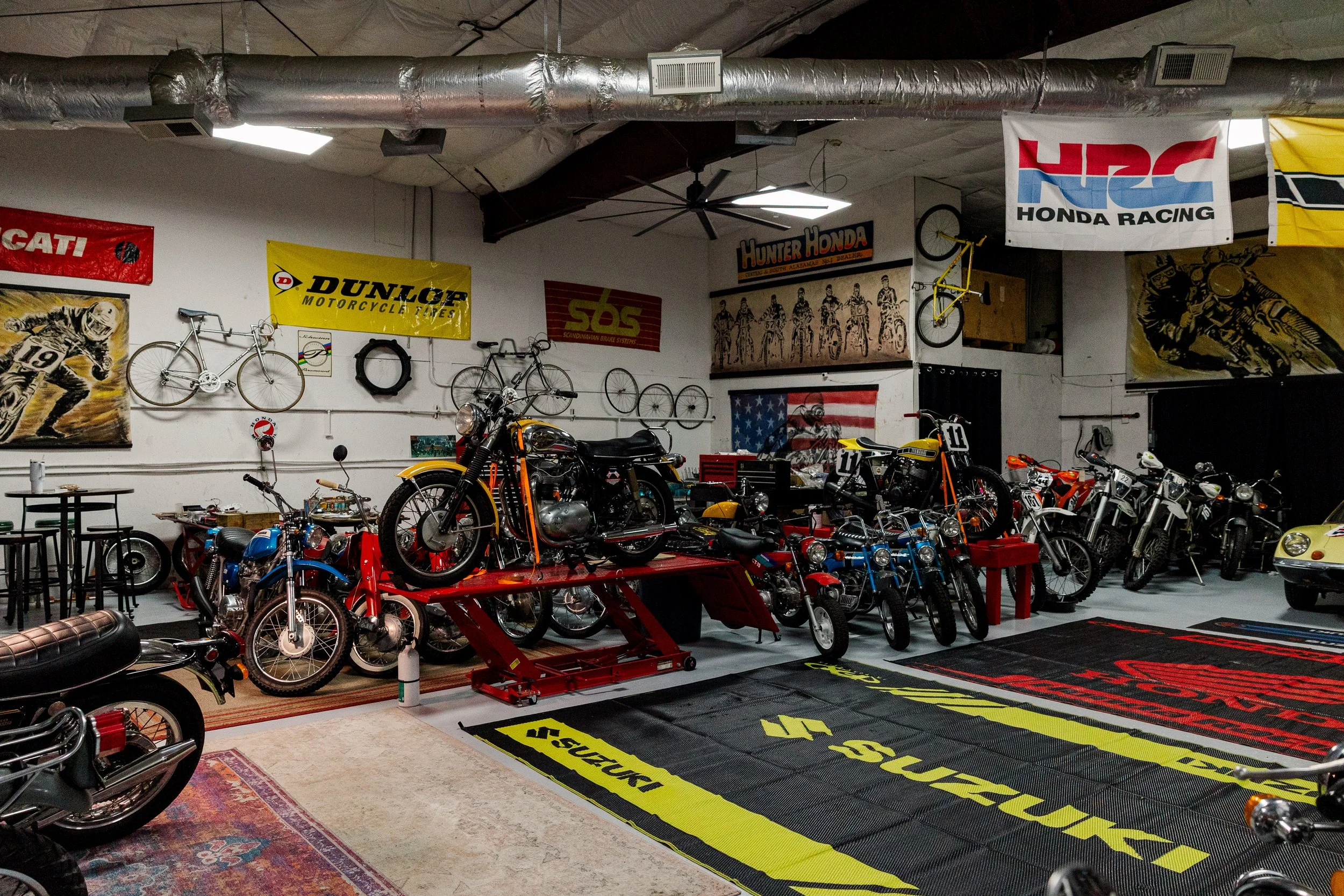 Collection of vintage motorcycles inside a garage with banners on the wall, including brands like Ducati, Dunlop, and Honda Racing. Vintage motorcycle collection on display at Birmingham Vintage Cycle in Birmingham Alabama