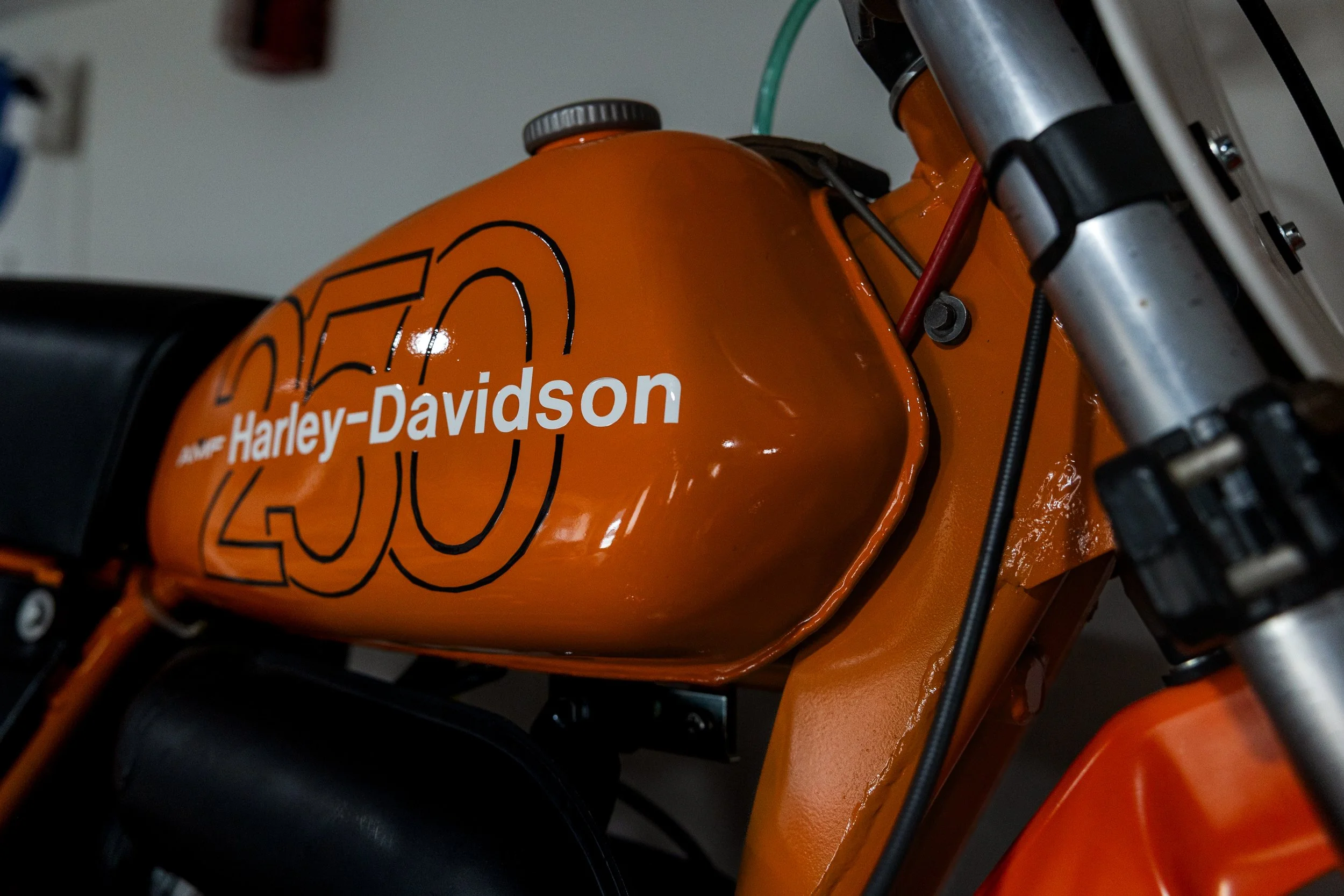 Close-up of an orange Harley-Davidson motorcycle fuel tank with black and white graphic design and a silver fuel cap. Vintage motorcycle detail at Birmingham Vintage Cycle, a vintage motorcycle restoration shop in Birmingham Alabama