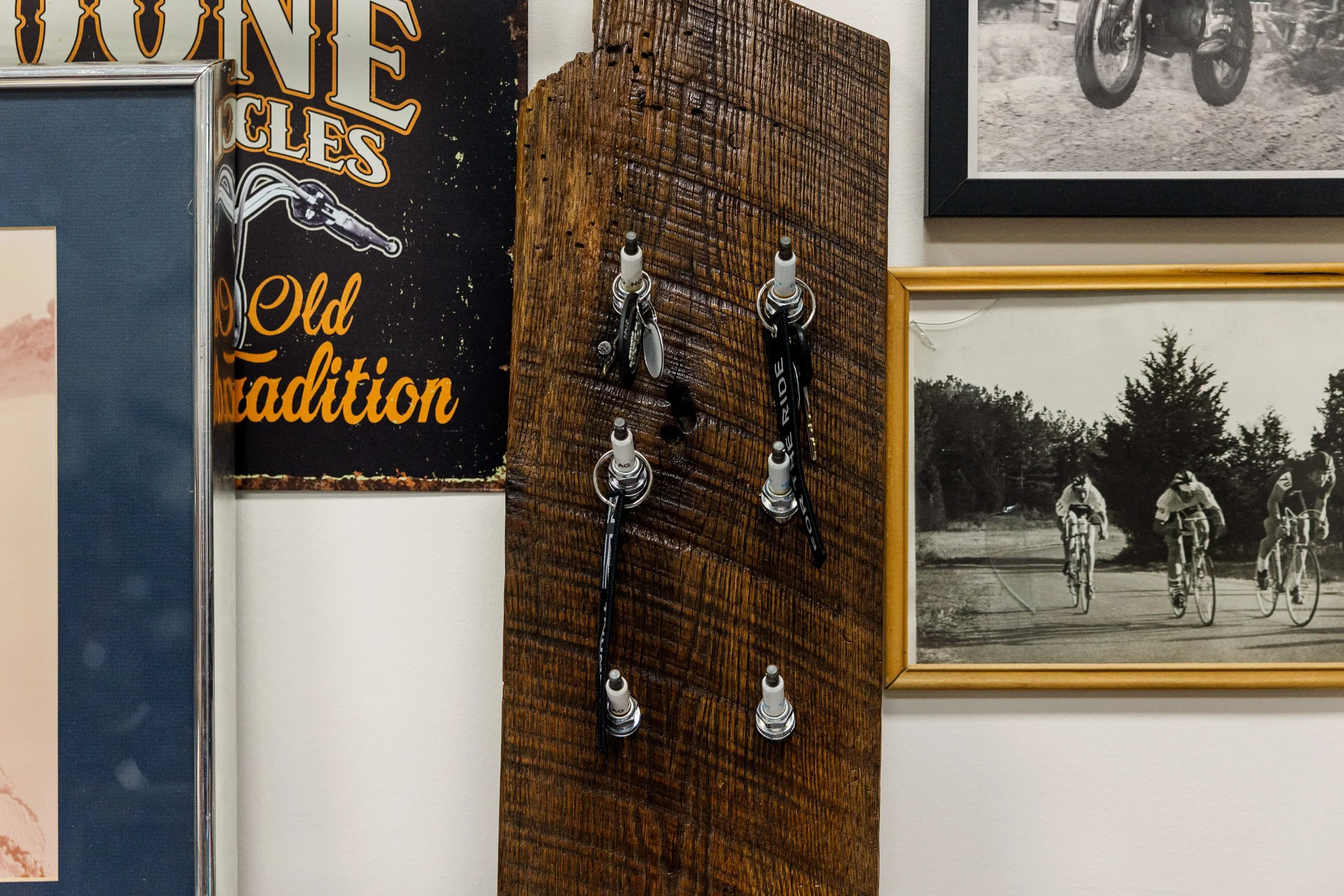 Wall decor with vintage bicycle and motorcycle photos, a wooden key holder panel with hooks, and a sign that says "Old Tradition". Inside Birmingham Vintage Cycle, a vintage motorcycle shop and community space in Birmingham Alabama