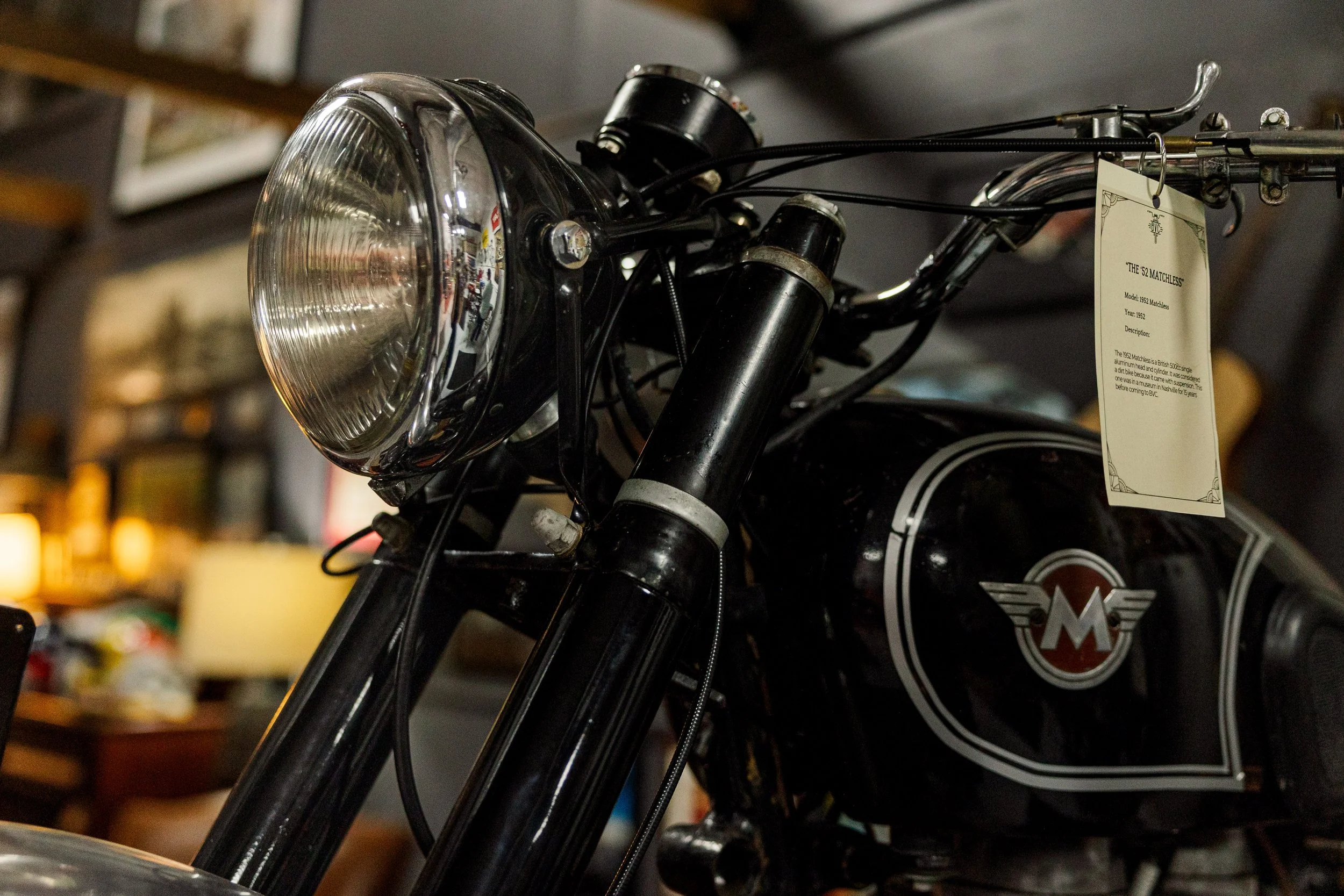 Close-up of the front headlight and handlebars of a vintage motorcycle with a tag attached to the handlebar. Vintage motorcycle detail at Birmingham Vintage Cycle, a vintage motorcycle restoration shop in Birmingham Alabama