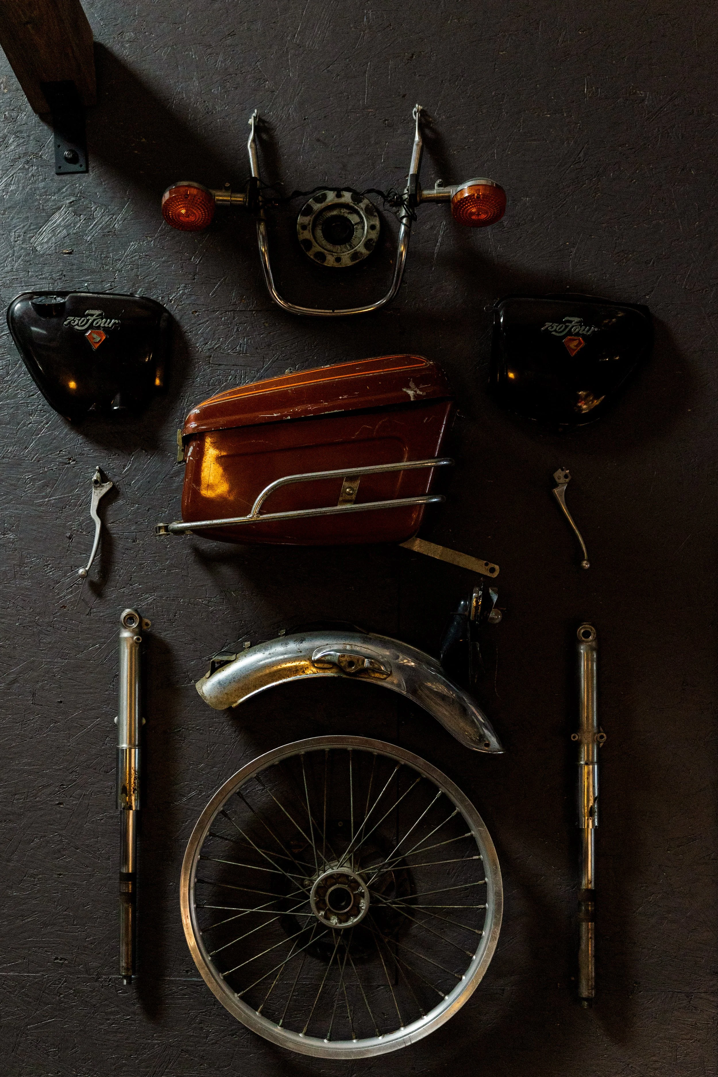 Disassembled vintage motorcycle with detached front wheel, fenders, and side covers on a black textured floor. Vintage motorcycle collection on display at Birmingham Vintage Cycle in Birmingham Alabama