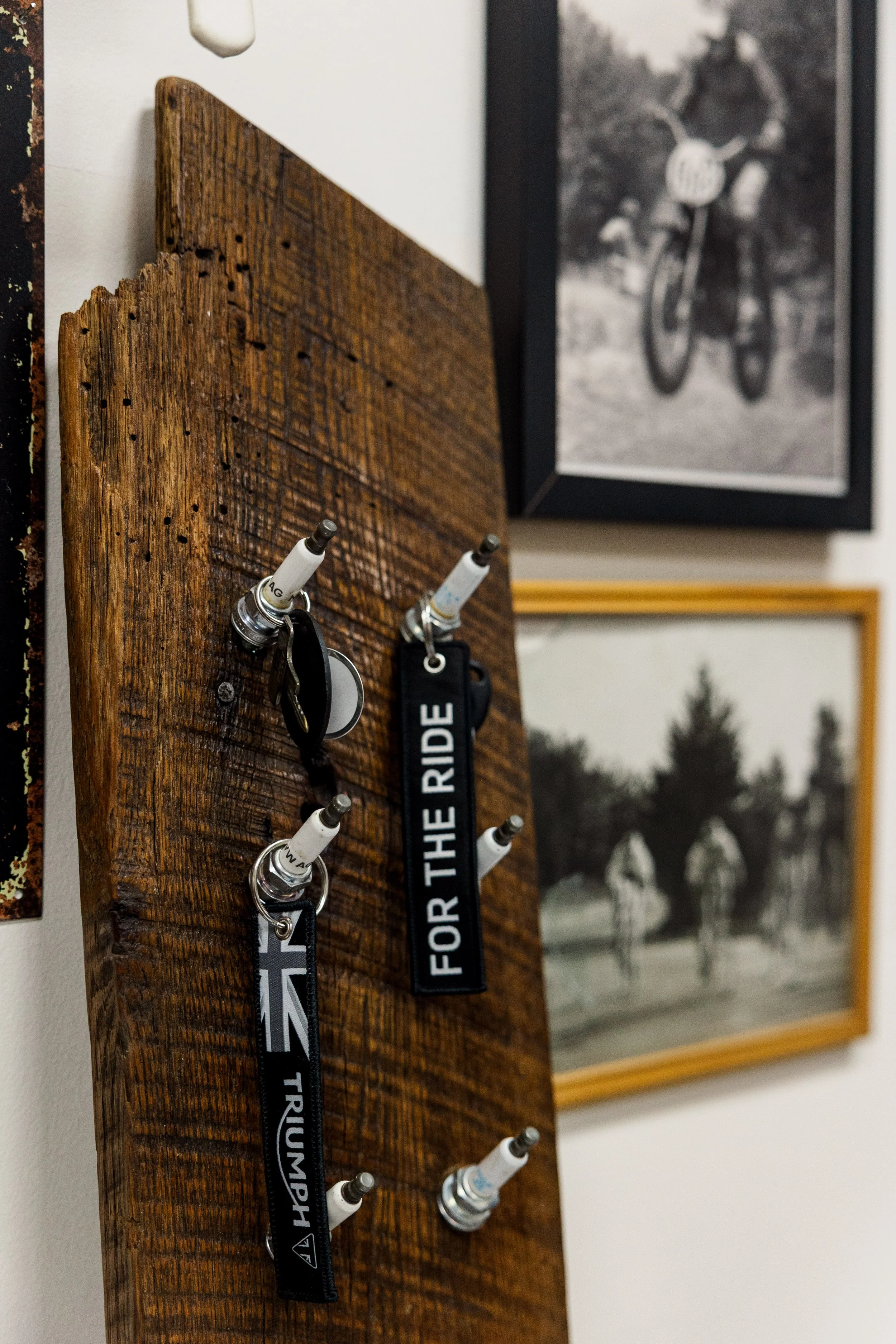 Close-up of a wooden board with four white markers and keychains attached, with framed black-and-white photographs in the background. Inside Birmingham Vintage Cycle, a vintage motorcycle shop and community space in Birmingham Alabama