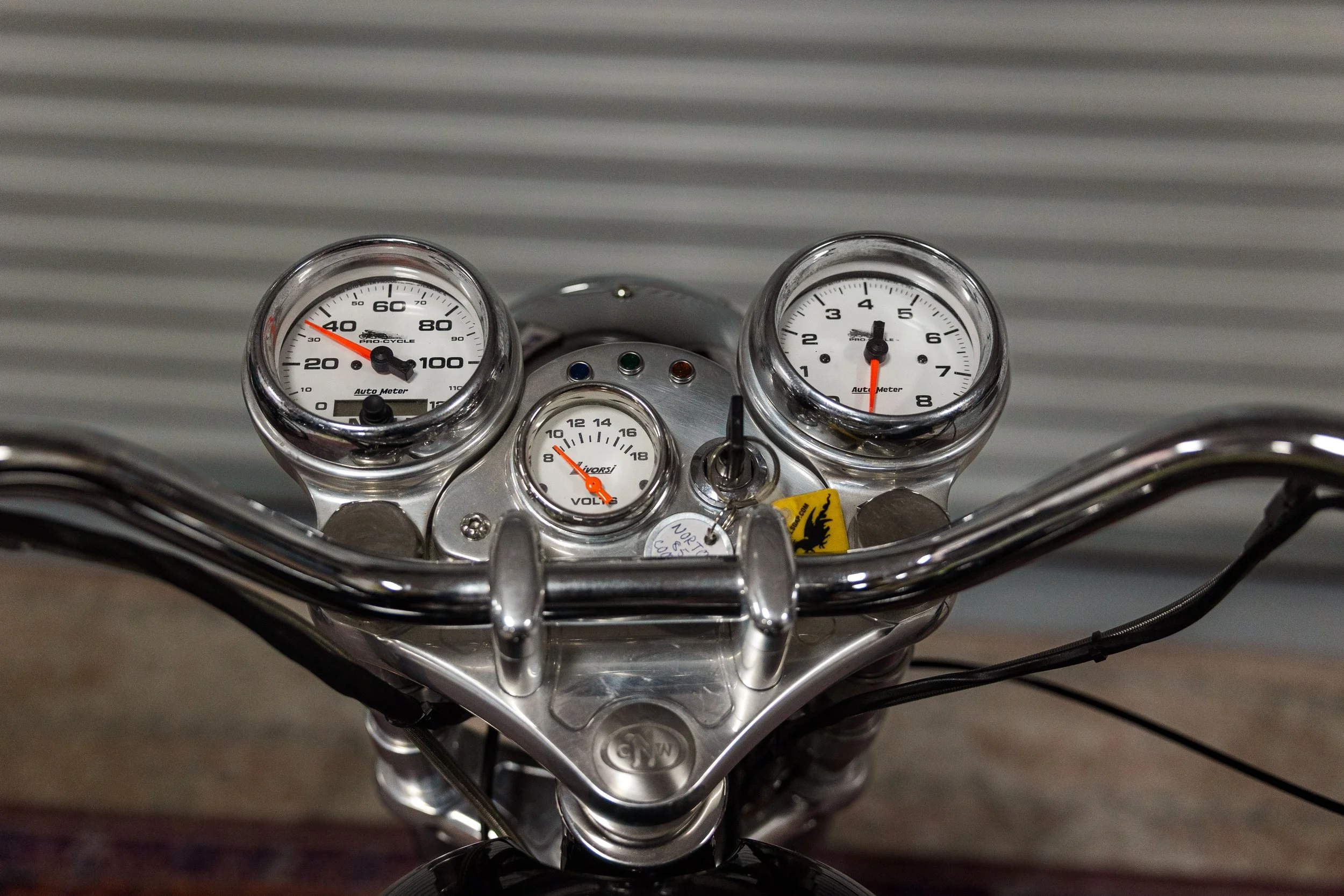 Close-up of motorcycle dashboard with speedometer, tachometer, and other gauges, with a corrugated metal background. Vintage motorcycle detail at Birmingham Vintage Cycle, a vintage motorcycle restoration shop in Birmingham Alabama