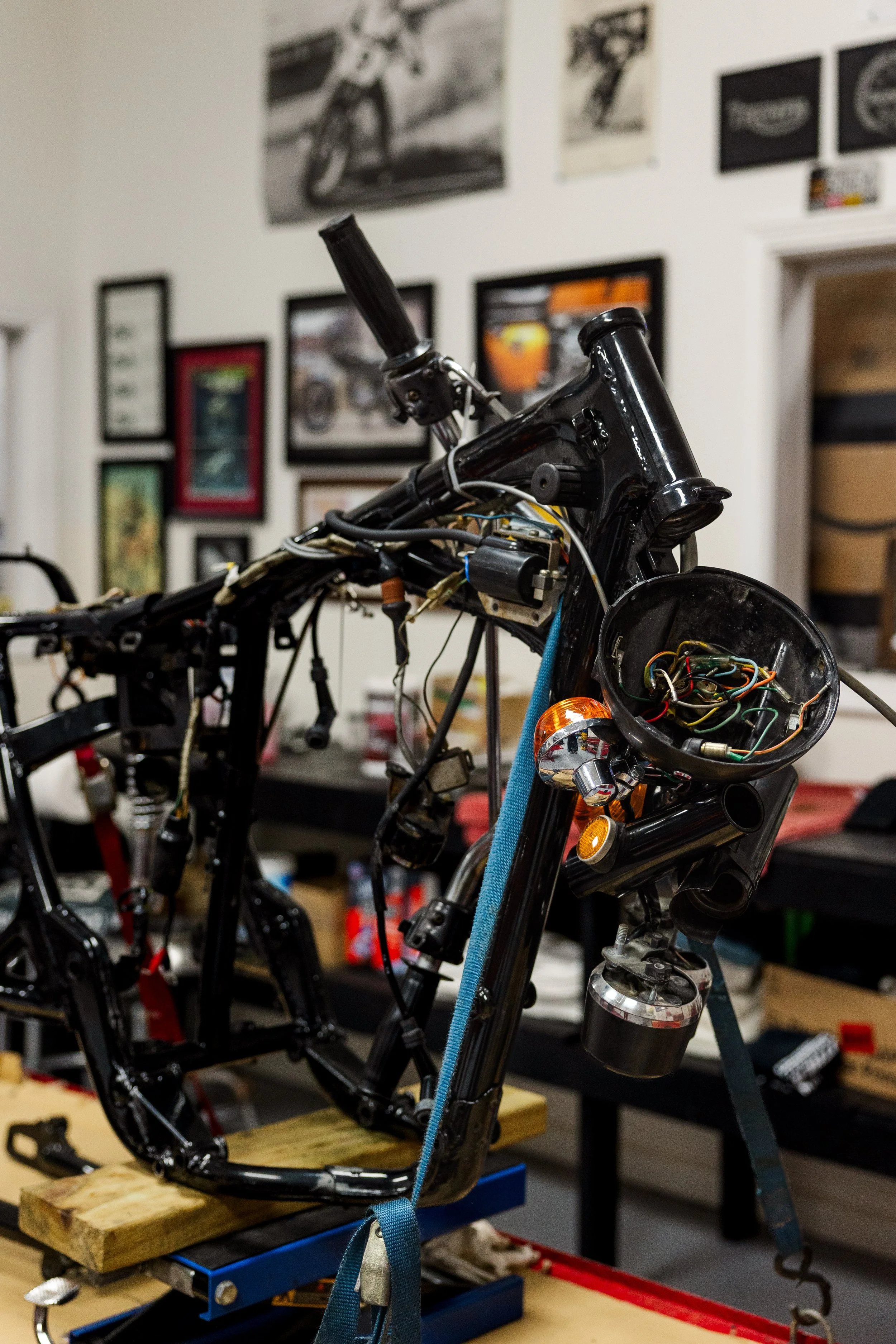 An unfinished motorcycle frame on a workbench, with wiring and components being assembled, in a workshop with framed pictures on the wall. Vintage motorcycle collection on display at Birmingham Vintage Cycle in Birmingham Alabama
