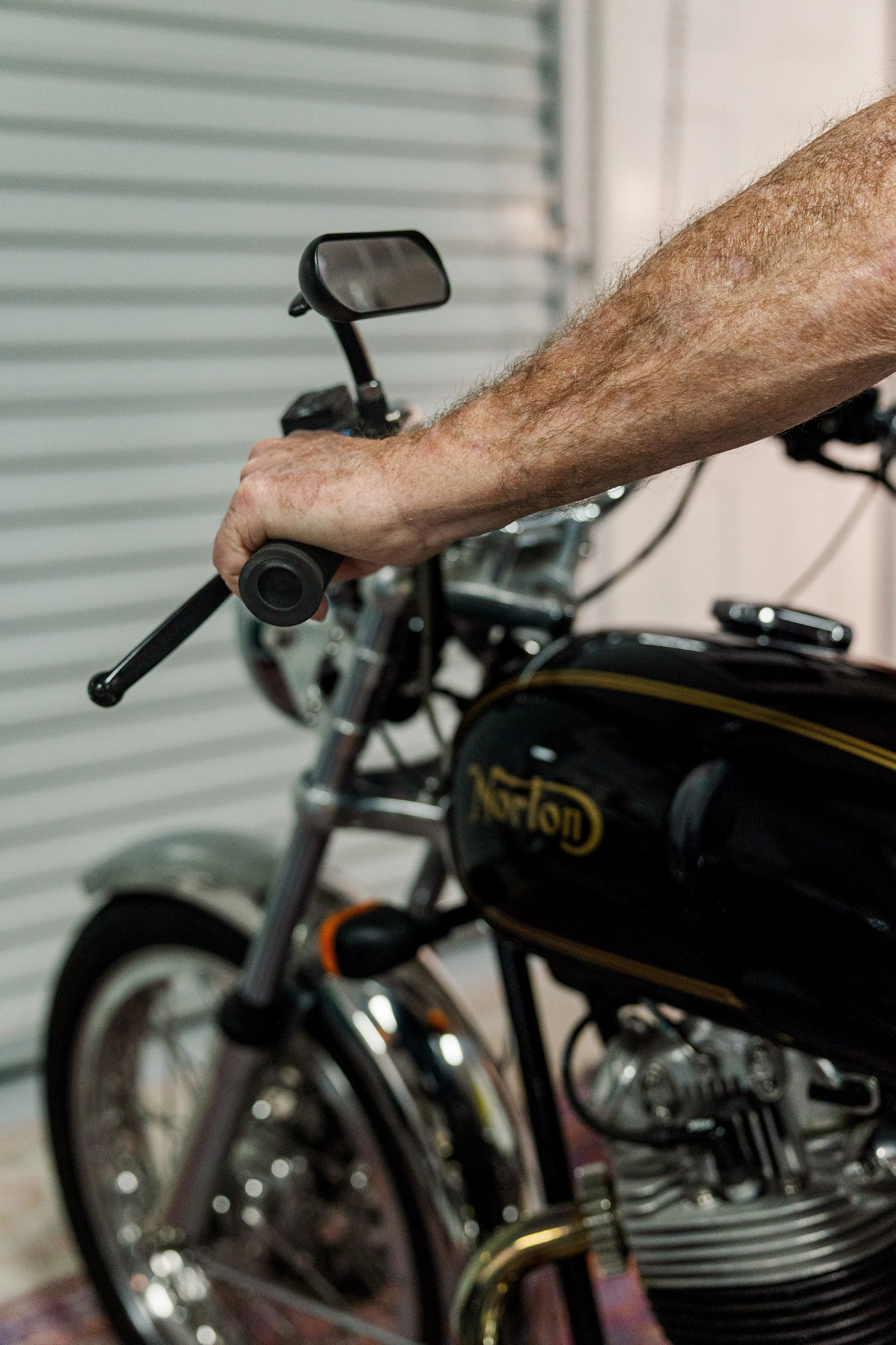 Close-up of a person's arm gripping the handlebar of a black motorcycle. Vintage motorcycle detail at Birmingham Vintage Cycle, a vintage motorcycle restoration shop in Birmingham Alabama