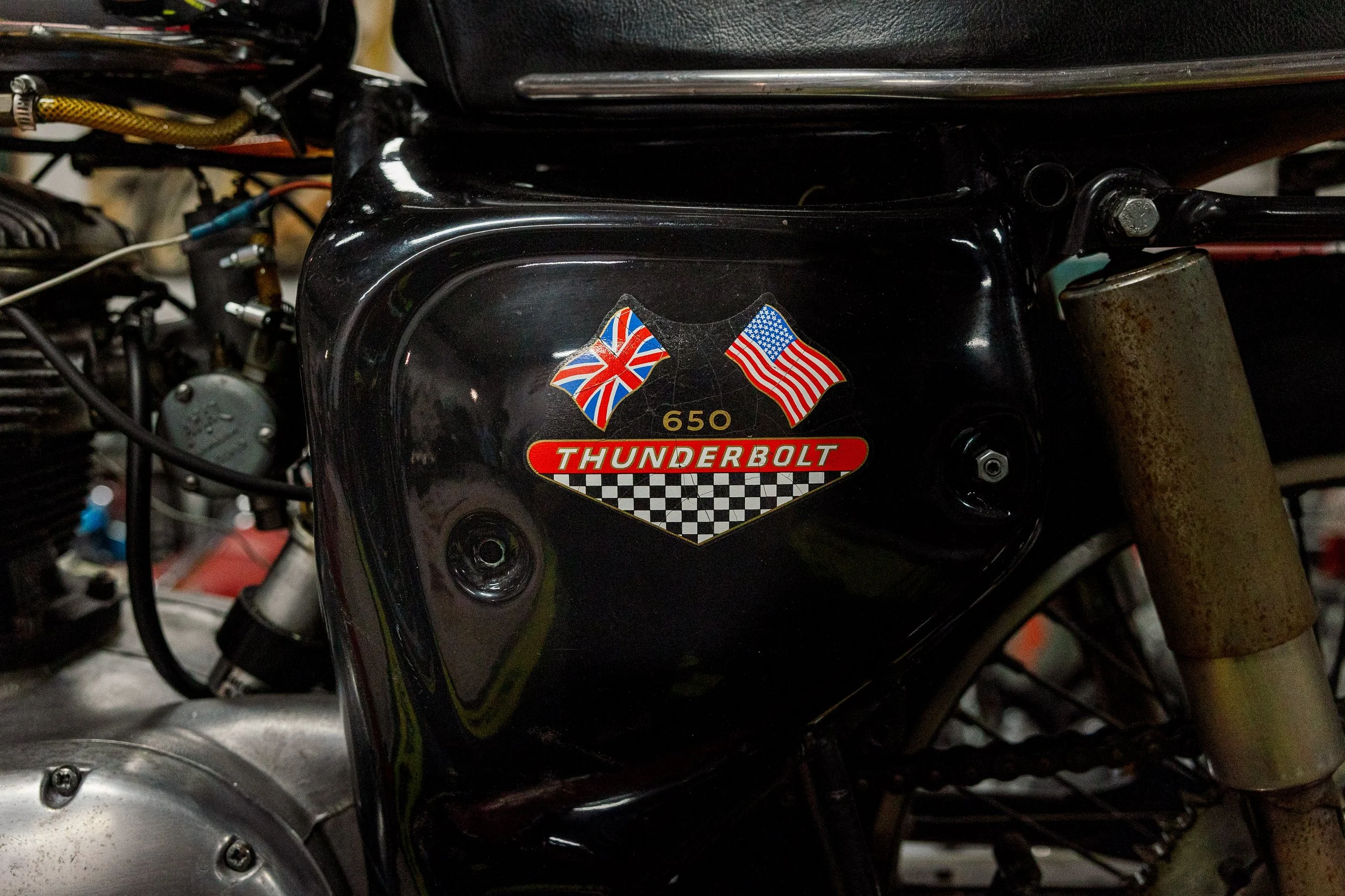 A vintage motorcycle tank with a sticker that has the British and American flags, the number 650, and the words "Thunderbolt" along with a checkered flag pattern. Vintage motorcycle collection on display at Birmingham Vintage Cycle in Birmingham