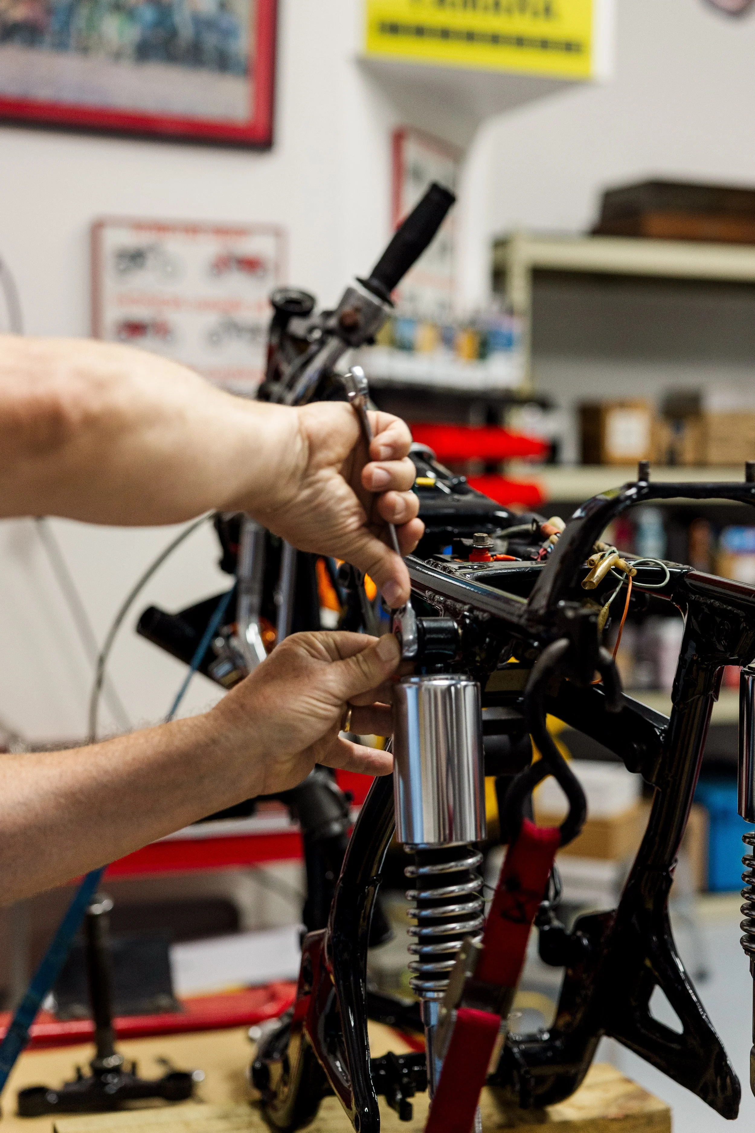 Person working on assembling a motorcycle frame in a workshop, with tools and parts on a workbench. Vintage motorcycle detail at Birmingham Vintage Cycle, a vintage motorcycle restoration shop in Birmingham Alabama
