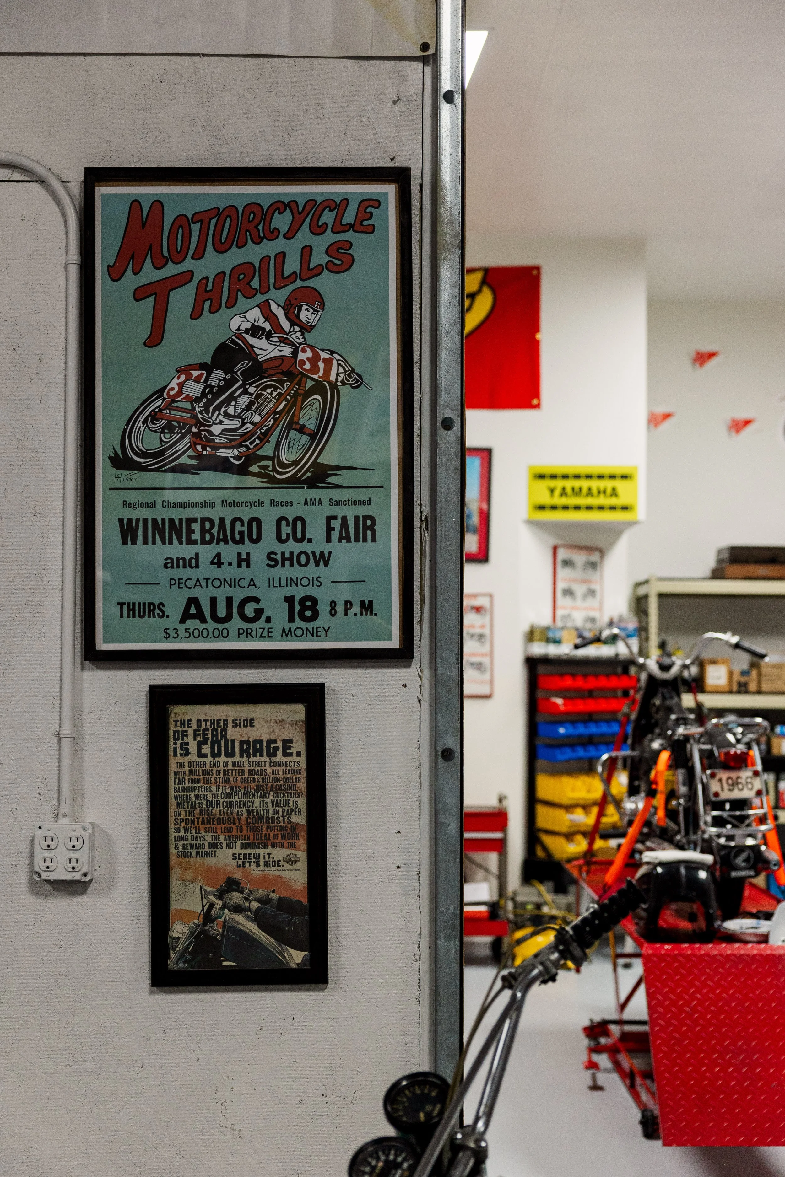 Poster on a wall advertising motorcycle races at Winnebago County Fair in Pecatonica, Illinois, on August 18 at 8 p.m., with a prize of $3,500.00. The poster features an illustration of a motorcycle racer. In the background, there is part of a motorc