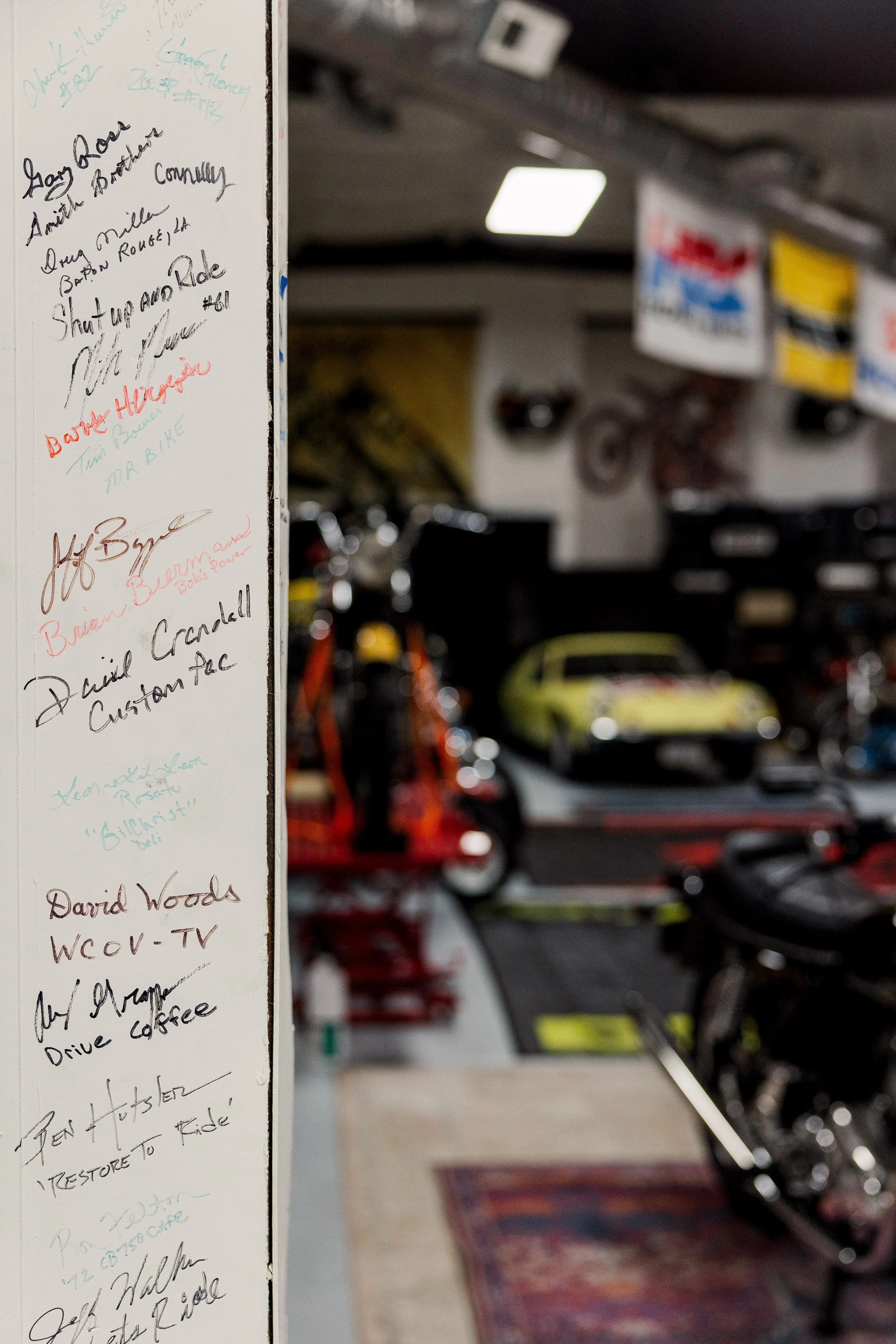 A whiteboard with handwritten notes on the left side of the image and a garage filled with various cars and race flags in the background on the right side.
