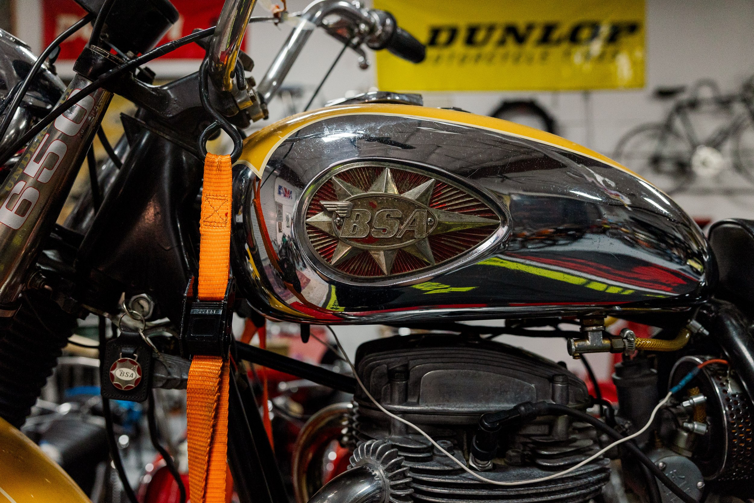 Close-up of a vintage BSA motorcycle engine and fuel tank with a shiny chrome finish, surrounded by various parts and wires, in a workshop setting. Vintage motorcycle collection on display at Birmingham Vintage Cycle in Birmingham Alabama