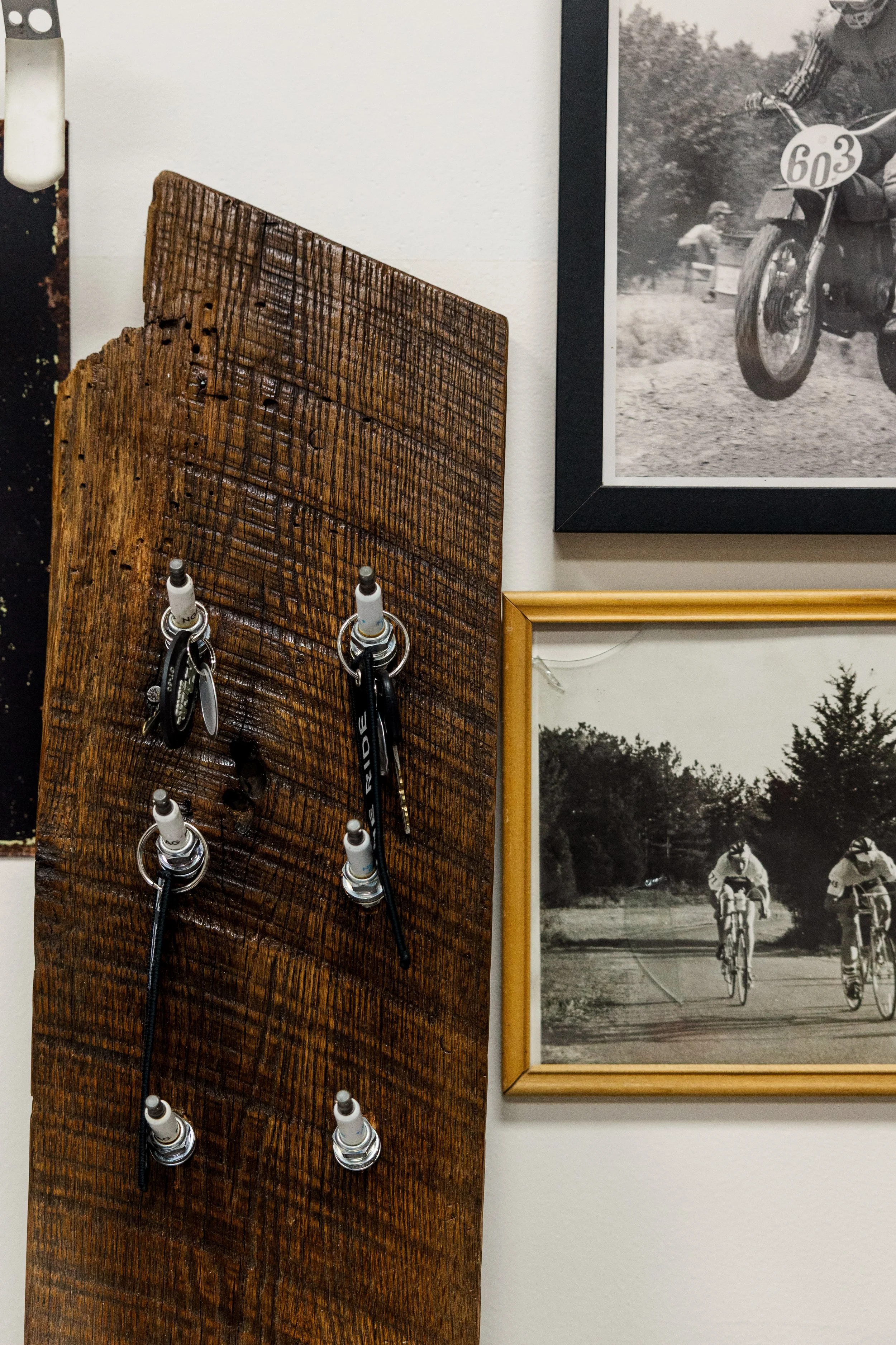 Close-up of a wooden display with six hanging bicycle keys and a black and white photograph of kids riding bikes in the background. Inside Birmingham Vintage Cycle, a vintage motorcycle shop and community space in Birmingham Alabama