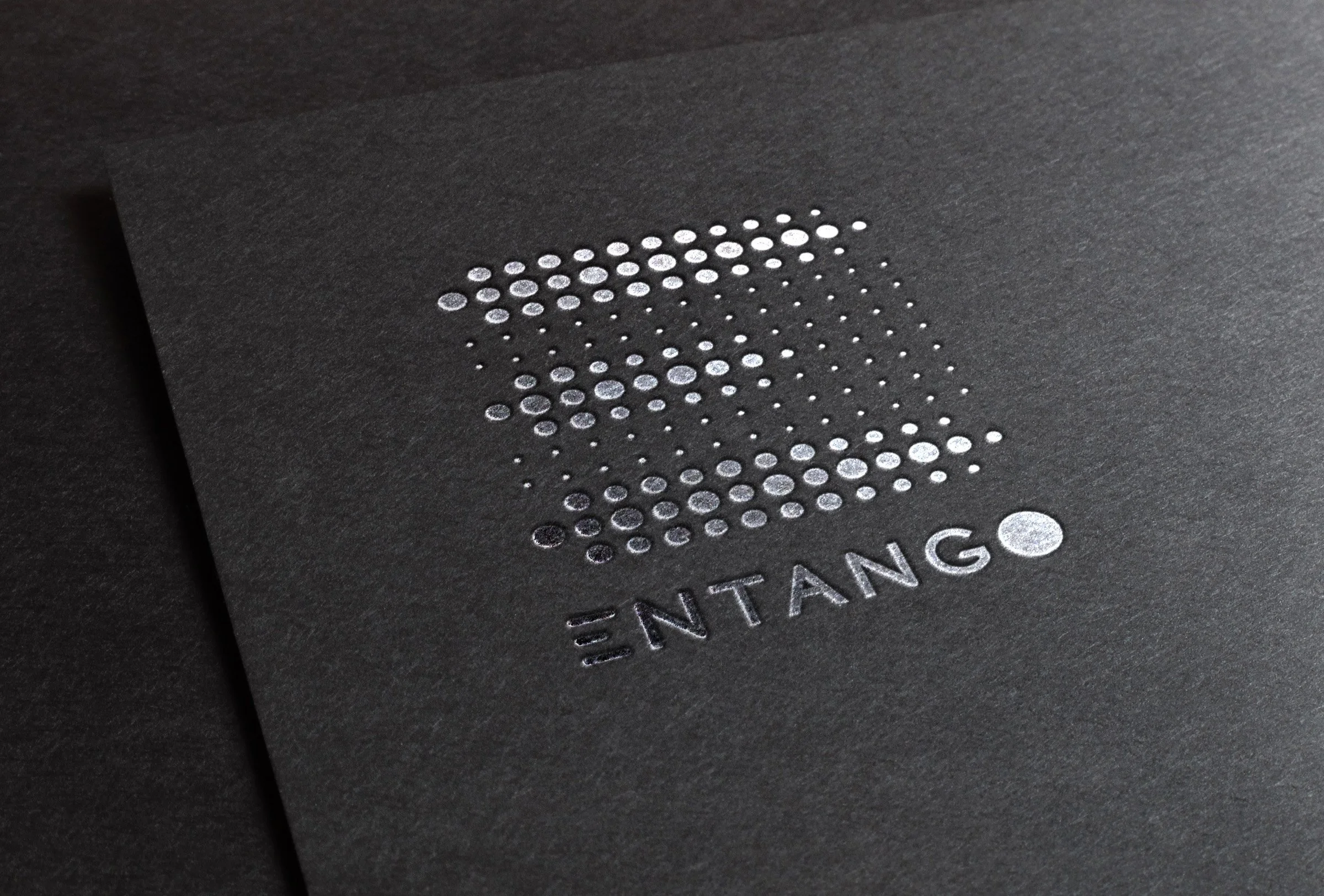 Close-up of black surface with word 'ENTANG' in silver and a pattern of silver dots forming a logo or design.