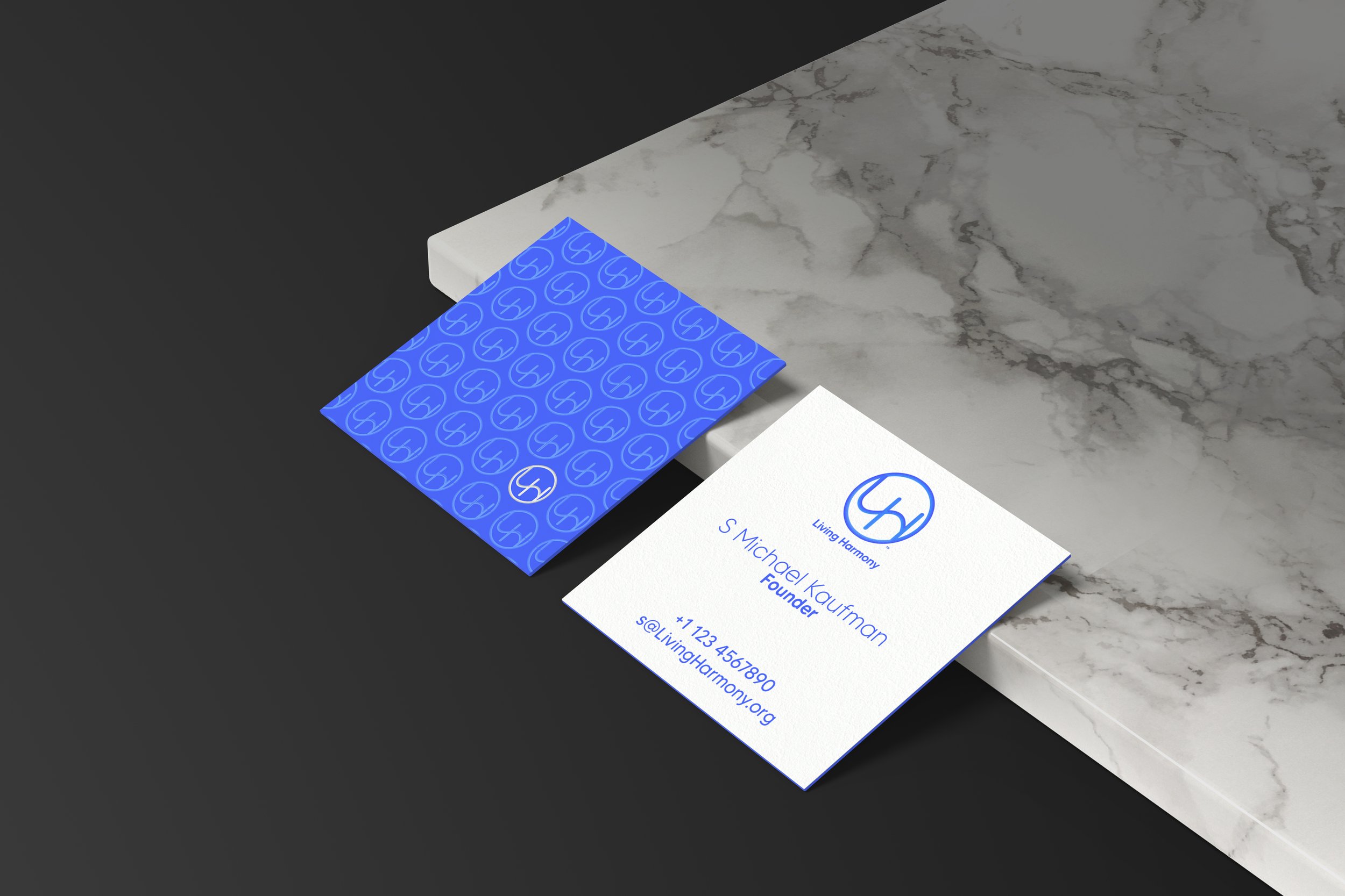 Business card for S. Michael Kaurman, founder, with contact info, placed near a blue patterned sticker and a black and white marble surface.