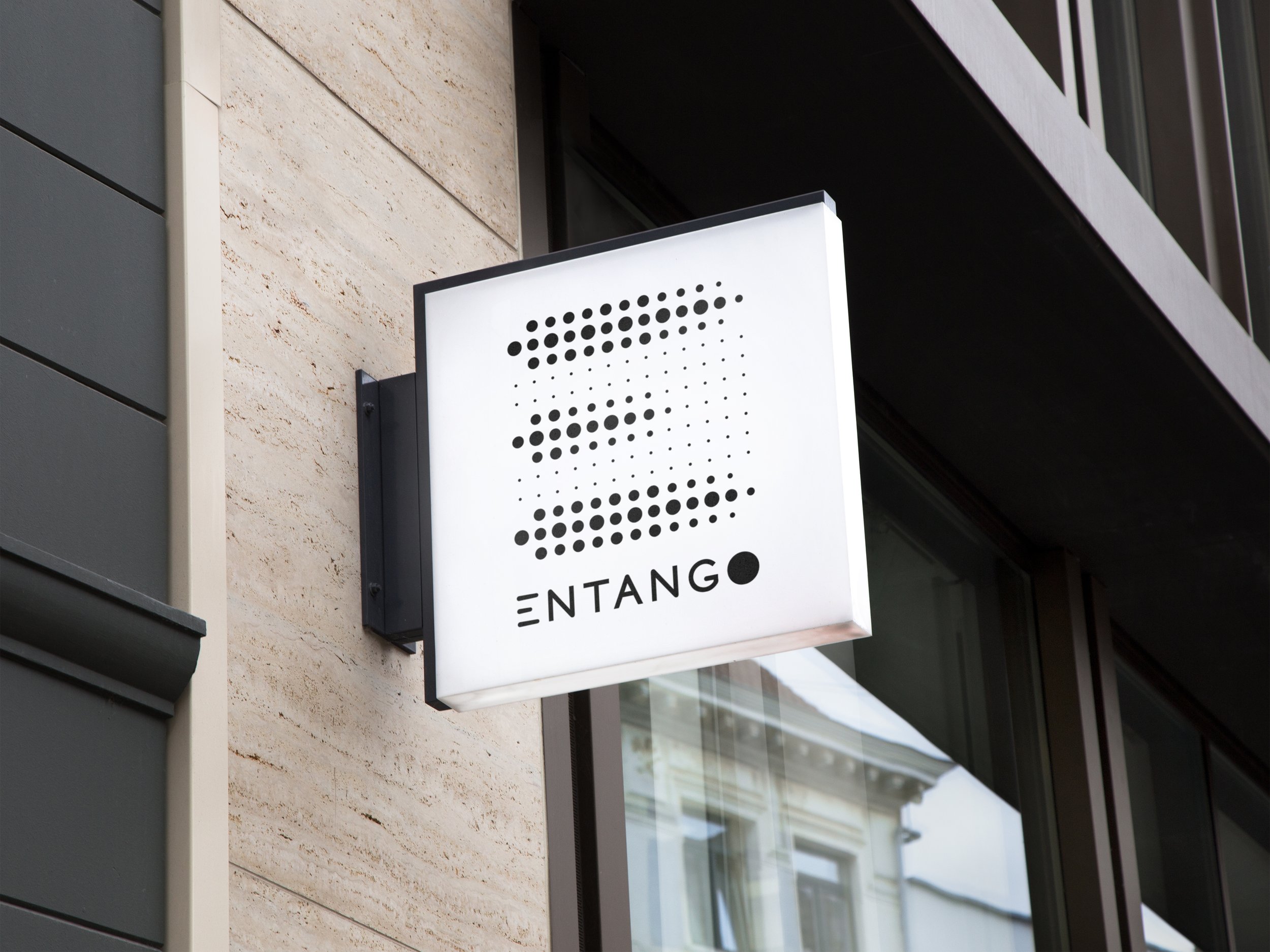 Close-up of a modern building exterior with a white sign featuring black dots arranged in the shape of a whale. The sign is attached to the wall near a large window.
