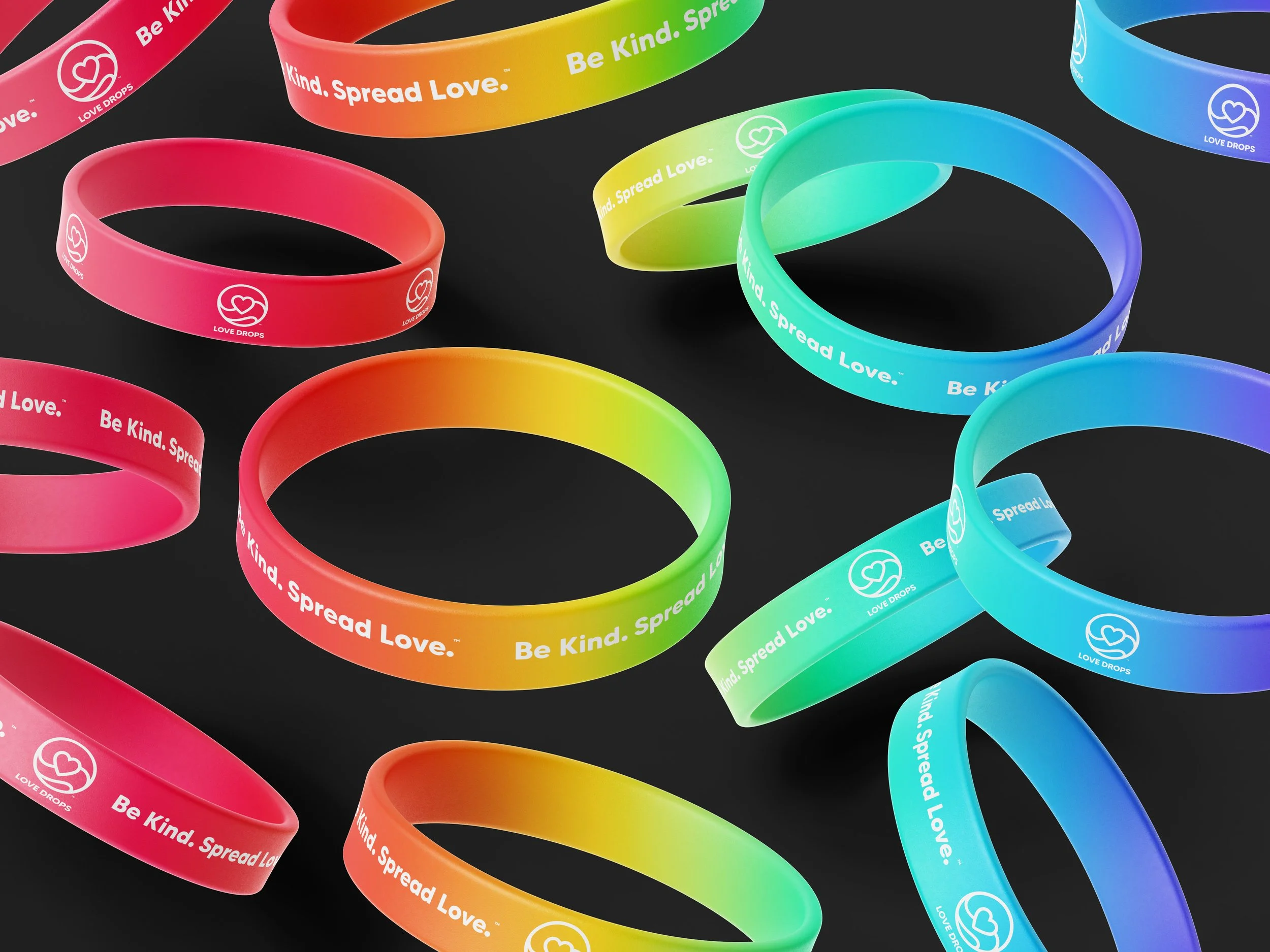 Colorful silicone wristbands with the message 'Be Kind. Spread Love.' and a heart logo, arranged on a dark background.