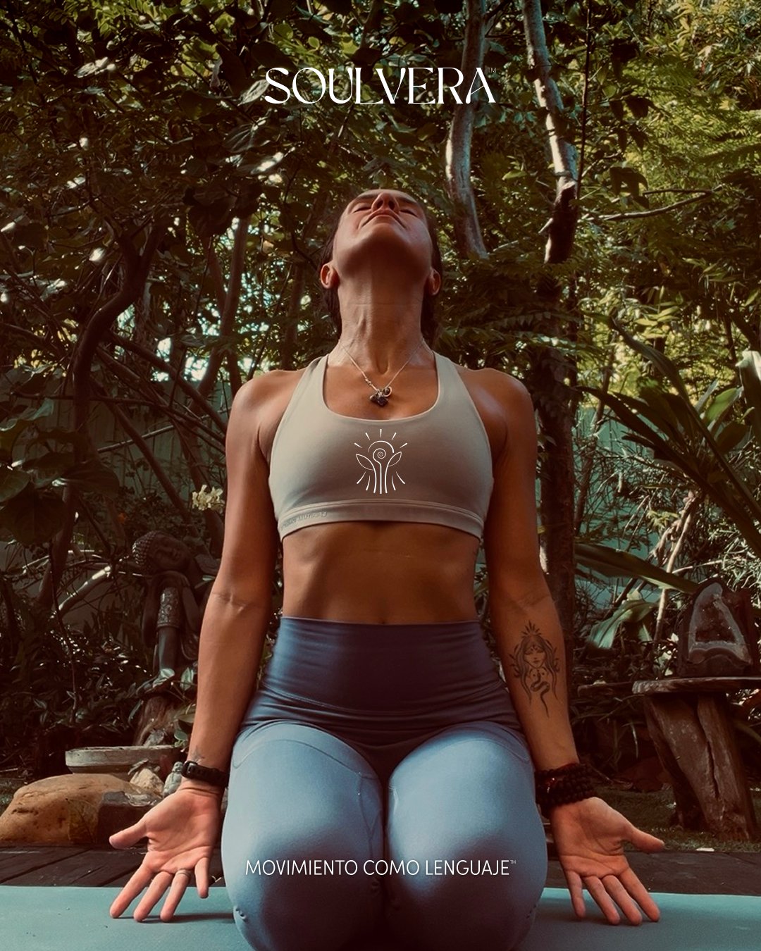 A woman practicing yoga outdoors surrounded by greenery, kneeling on a yoga mat in a meditative pose with her hands on the ground. She is wearing a light-colored sports bra and light blue leggings, with a tattoo on her left arm and a necklace. The words 'SOULVERA' and 'MOVIMIENTO COMO LENGUAJE' are displayed in the image.