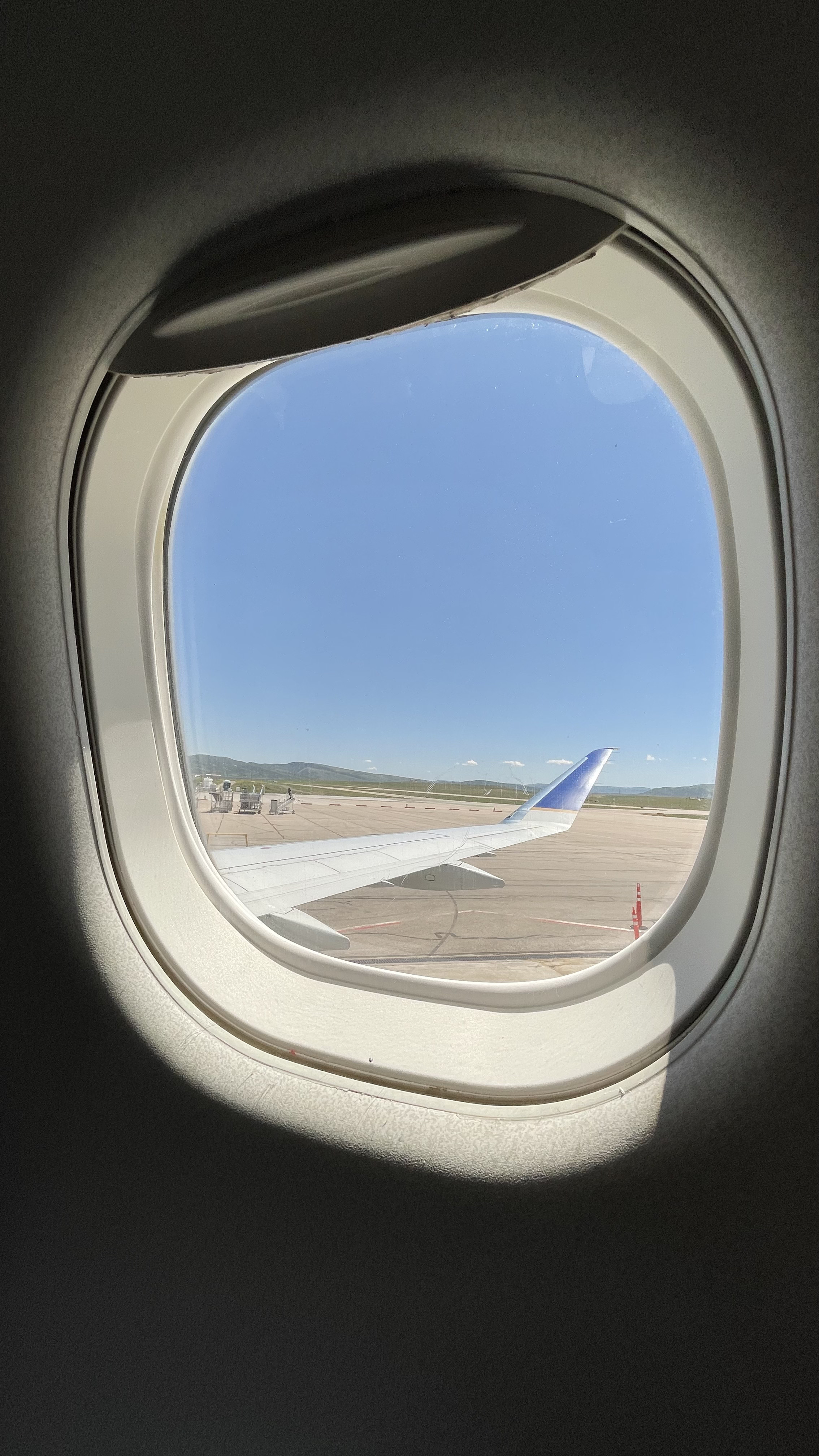 View of airplane wing outside the window of an airplane at an airport on a clear day.