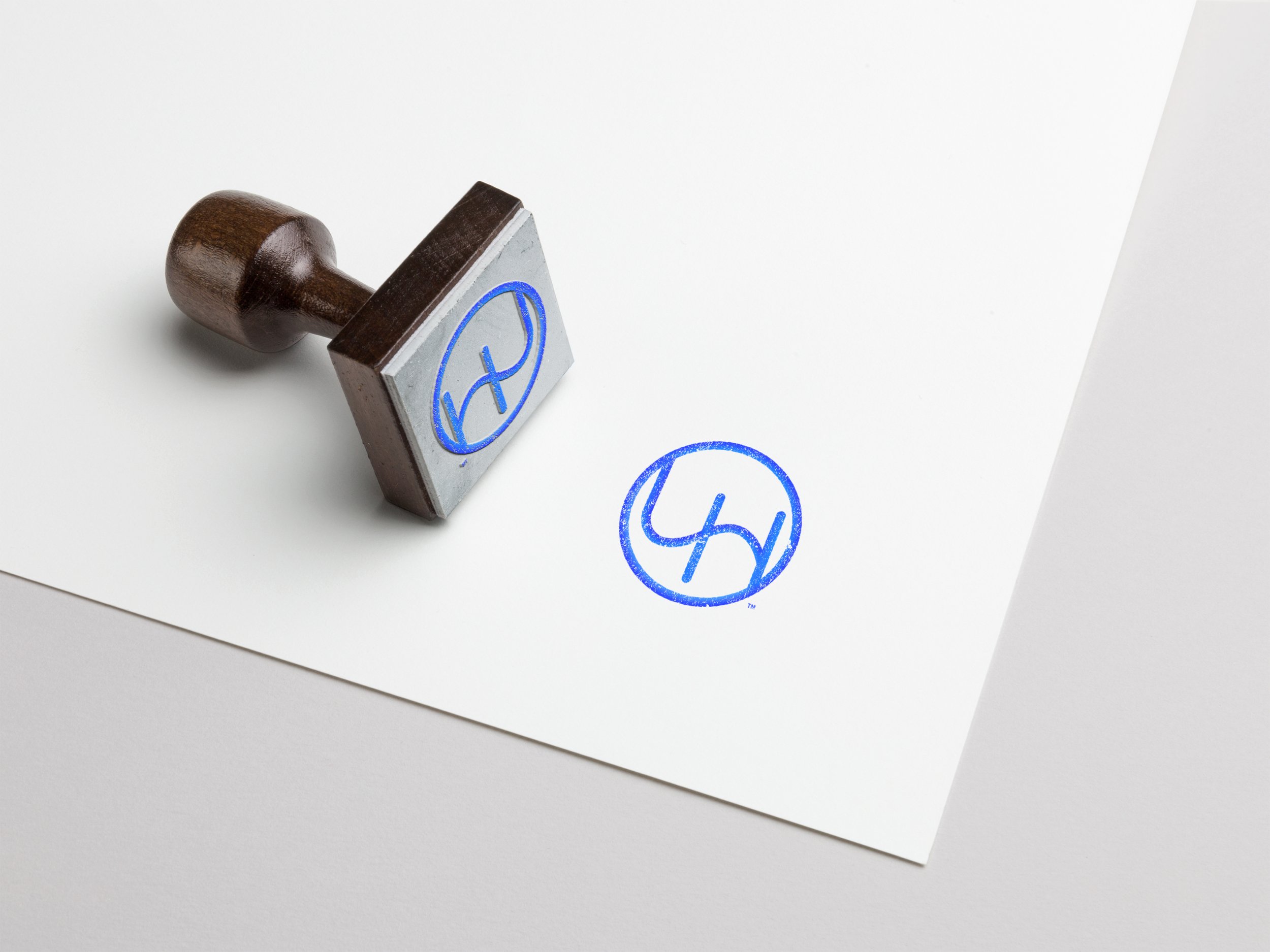 A rubber stamp with a wooden handle and a blue logo on the rubber part, stamping the logo onto a white sheet of paper.