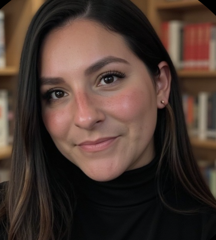 Close-up of a young woman with long dark hair and a warm smile, wearing a black turtleneck, with a bookshelf in the background.