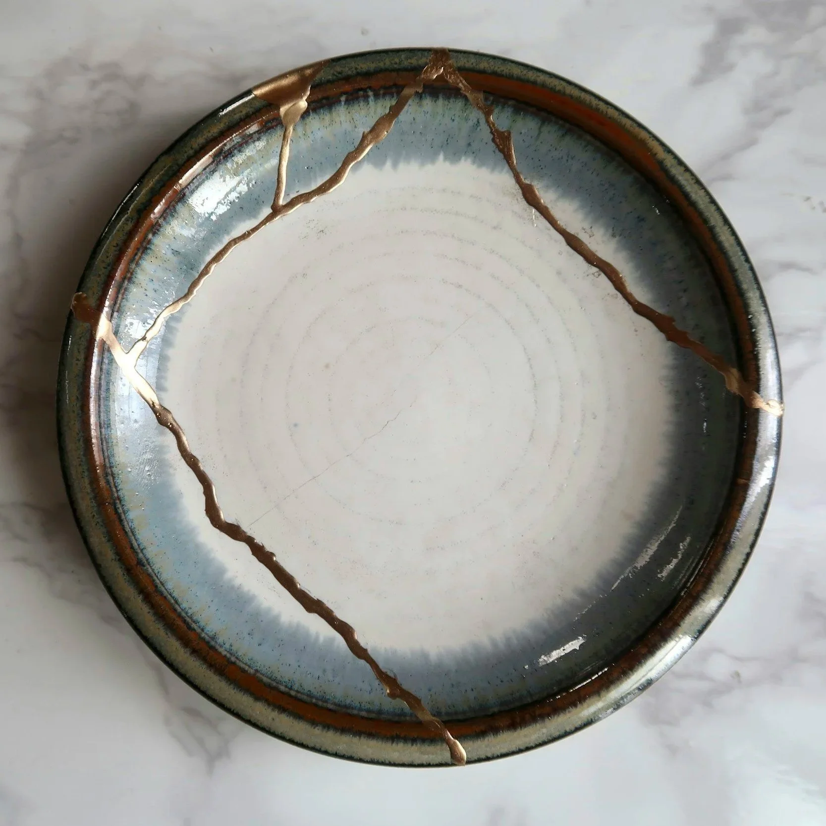 A ceramic plate with cracks and brownish-orange glaze lines on a marble surface.