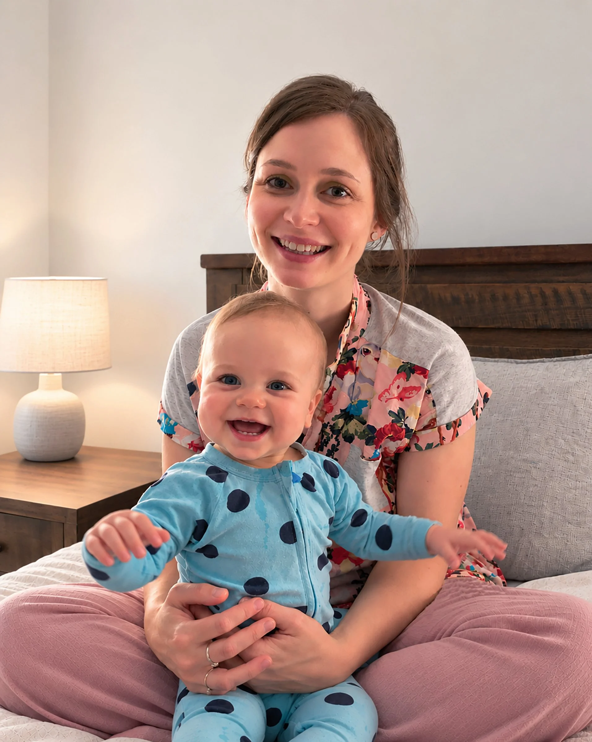 Smiling mother holding a happy baby in blue polka-dot pajamas on a bed