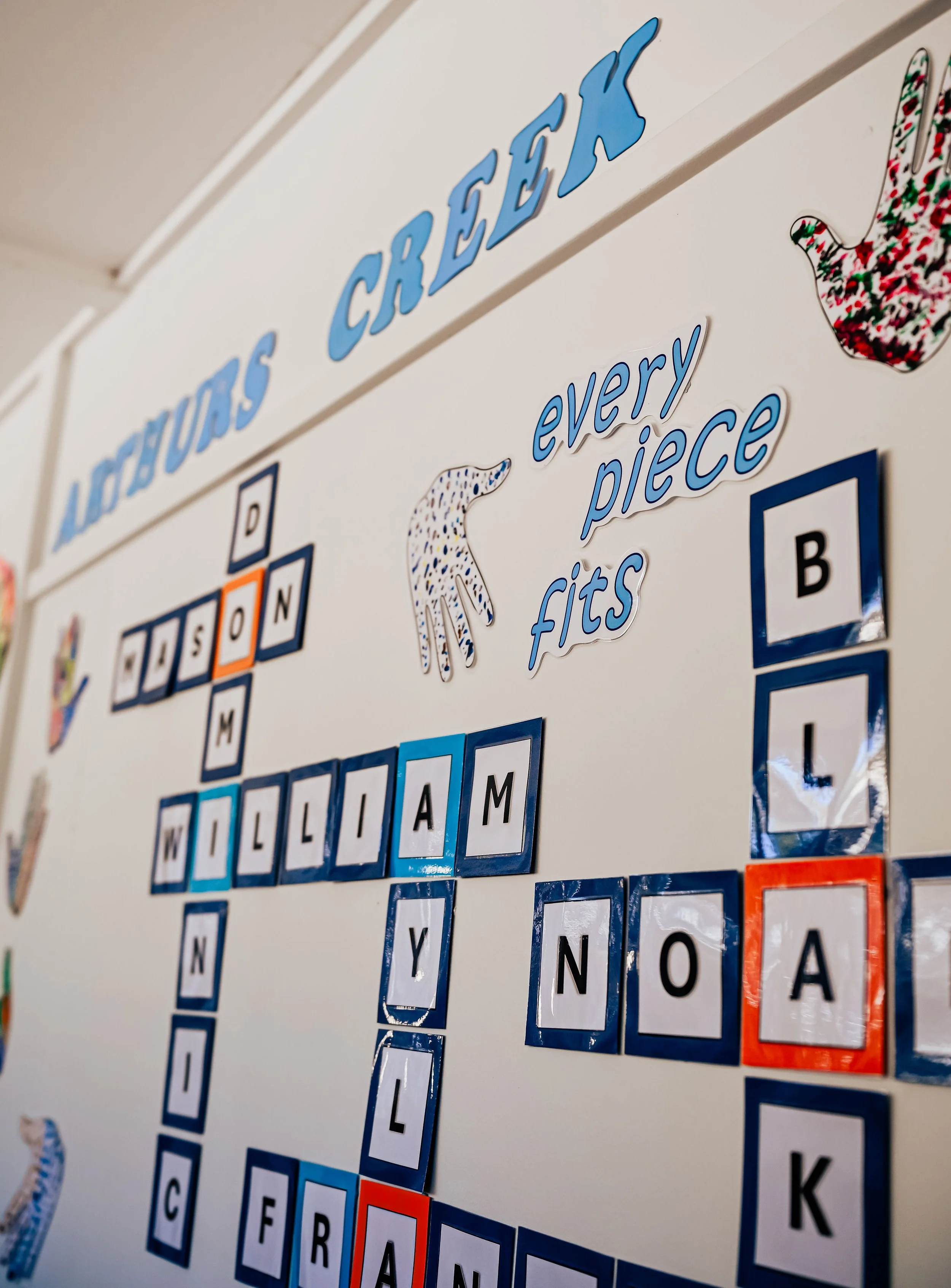 Classroom whiteboard with educational decorations, including the phrase 'every piece fits,' some illustrations of hands, and alphabet tiles arranged on the board.