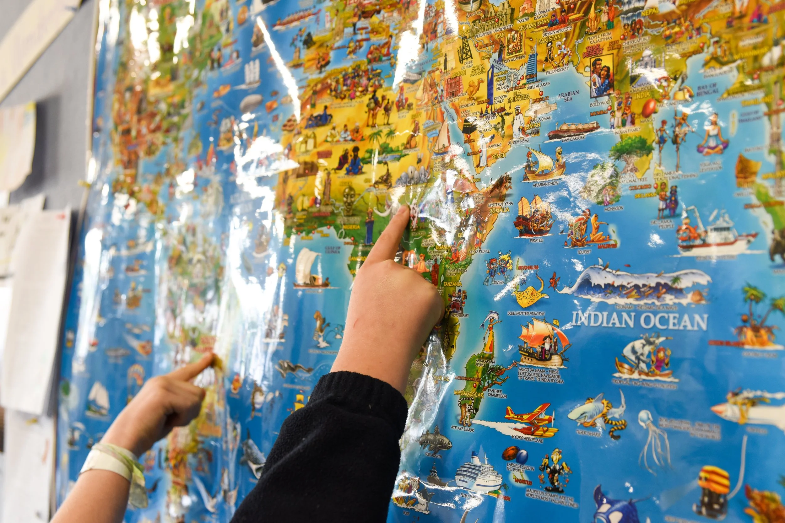 Children pointing at a colorful illustrated world map with various landmarks and regions.