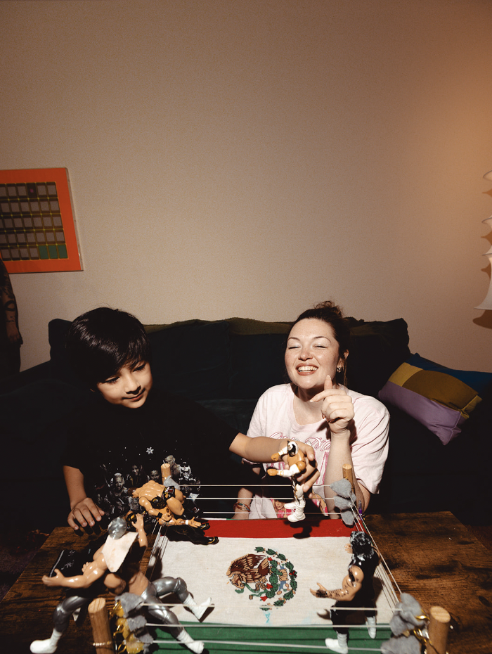 A young boy and a woman playing with a wrestling ring toy set, smiling and enjoying a game together in a cozy living room.