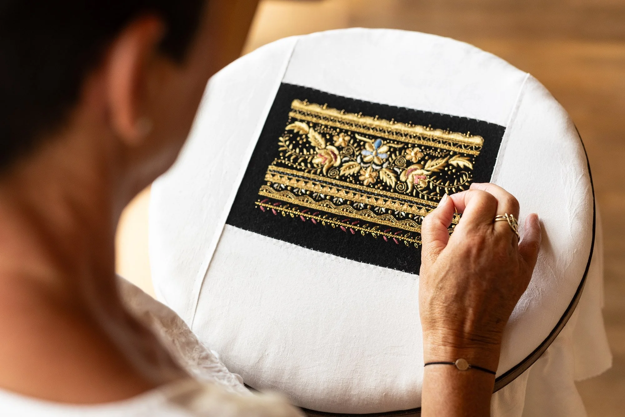 Frau näht auf einem weißen Stoffkörper mit gold- und silberverzierten Stickereien.