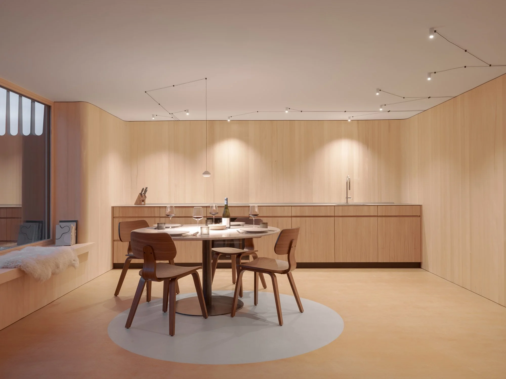 Moderner Essbereich mit runder Holztisch, vier Stühlen, Deckenleuchte, und Holzpaneel-Wand in einem minimalistischen Stil.
