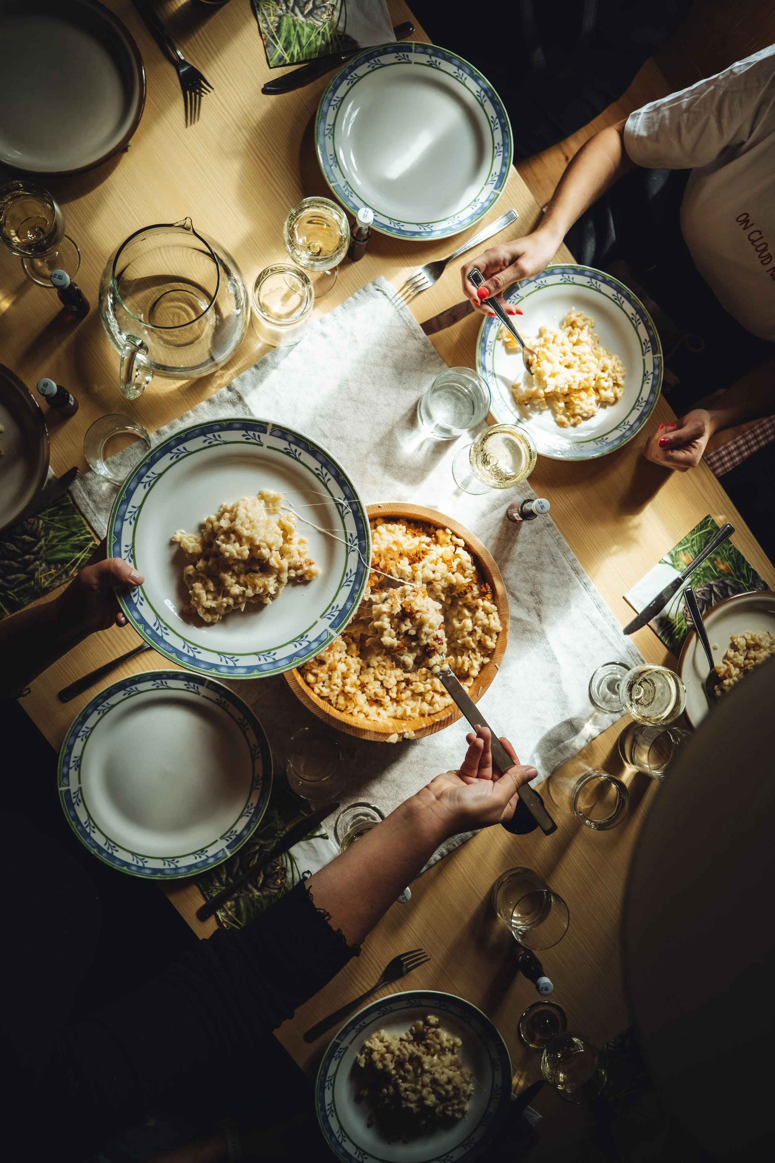 Tisch mit mehreren Tellern mit Risotto, mehreren leeren Tellern, Weingläsern, Wasserkrügen, Besteck und kleinen Fläschchen auf einer weißen Tischdecke, Menschen, die essen und servieren.