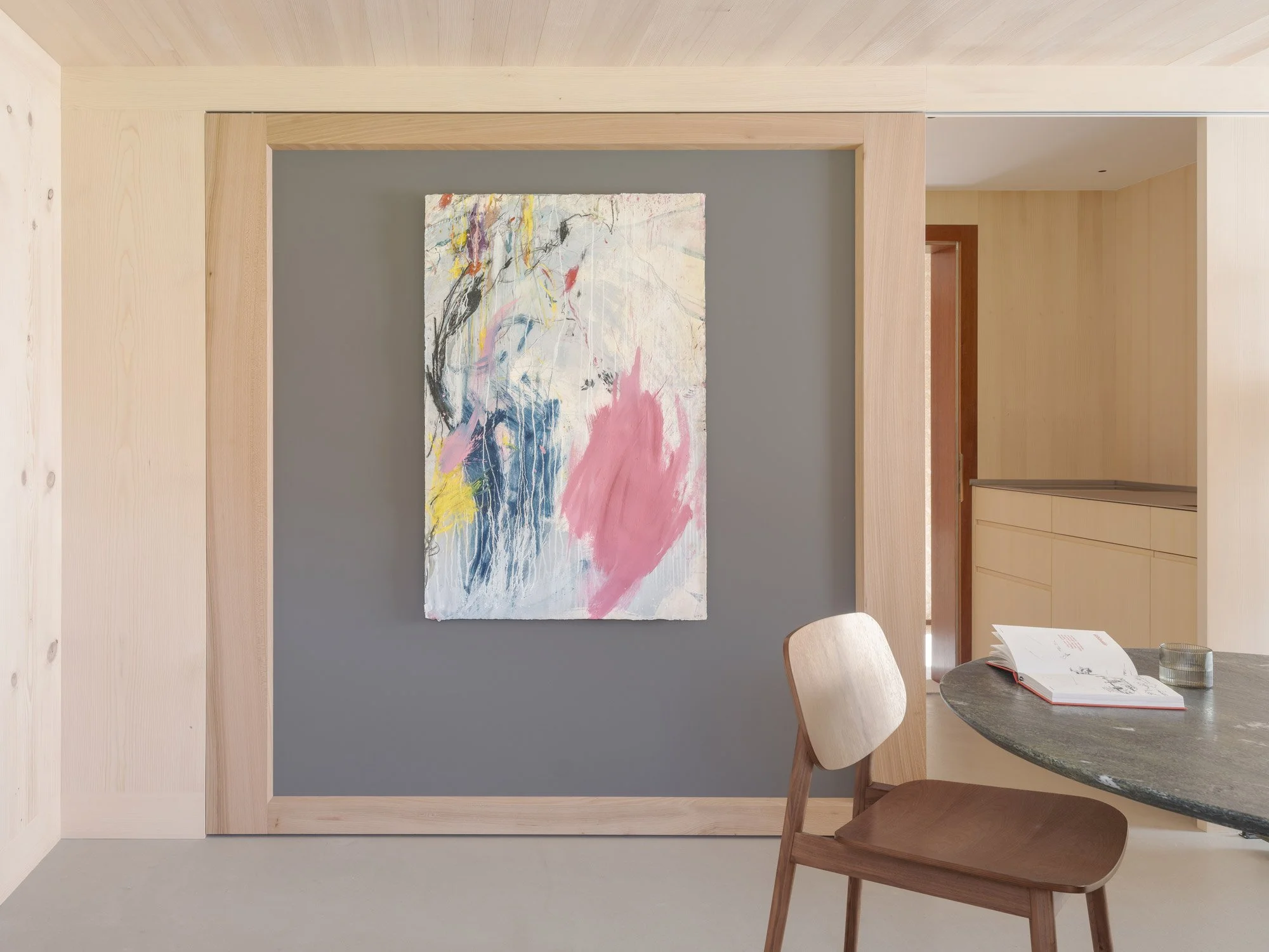 Moderner Kunstraum mit abstrakter Gemälde auf grauer Wand, Holzrahmen und schlichtem Holzinterieur.