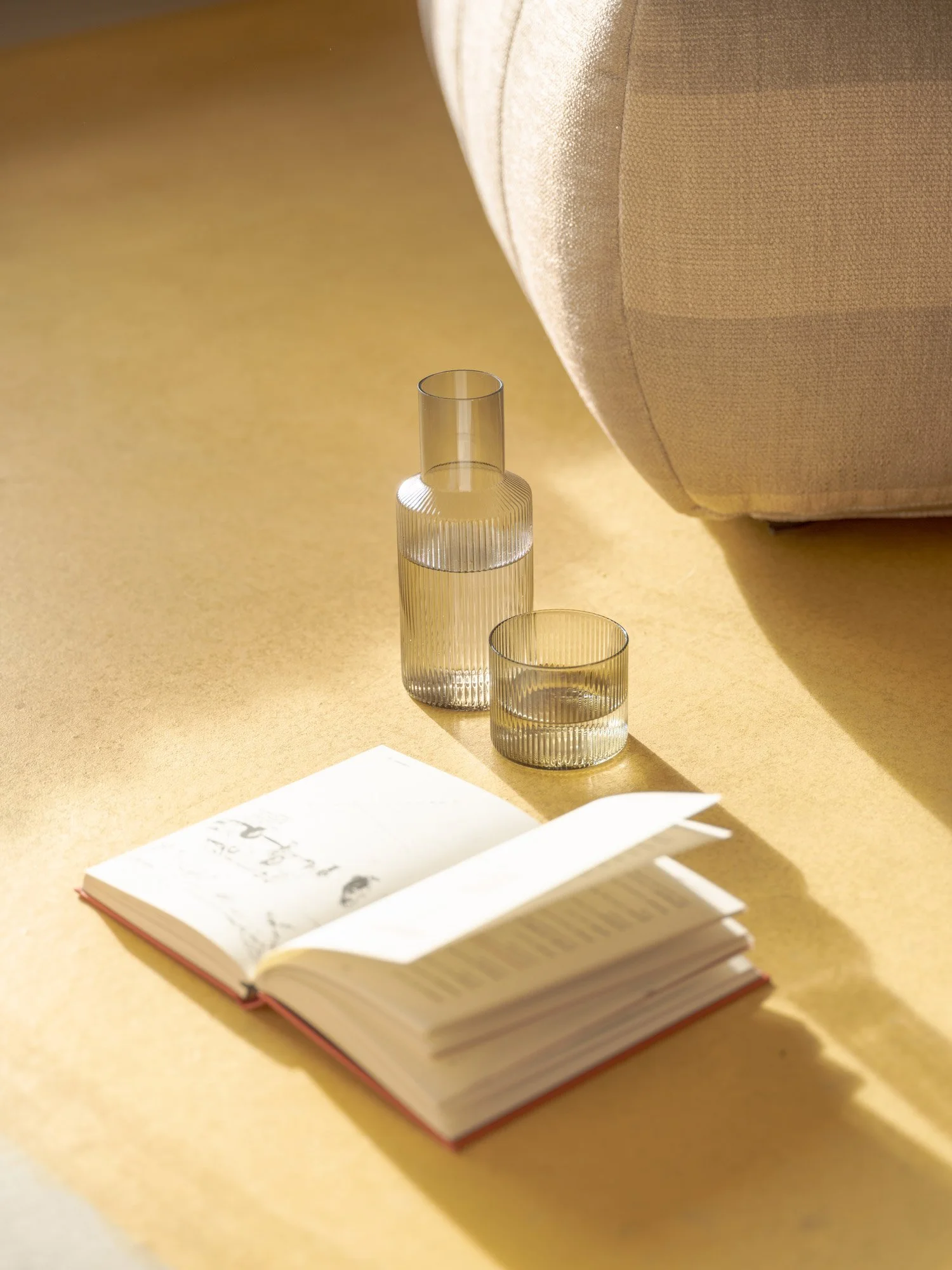 Ein aufgeschlagenes Notizbuch auf einem Tisch mit schwarzer Tinte auf weißen Seiten, daneben befinden sich drei transparente Glasvasen unterschiedlicher Höhe, die vor einem beige-farbenen Sofa stehen.
