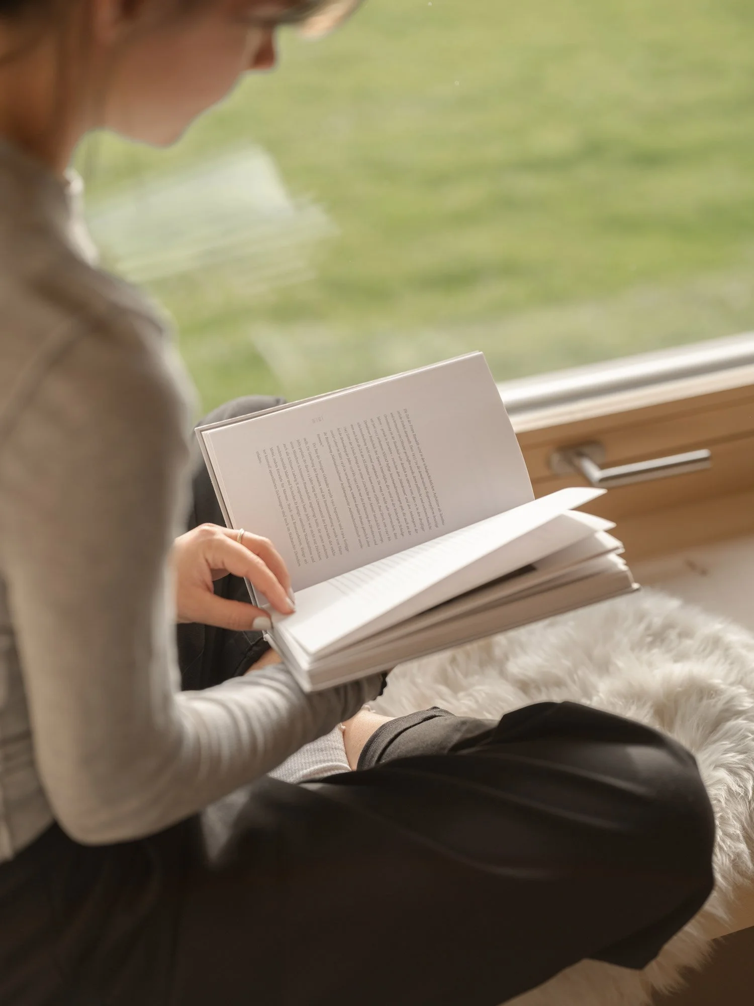 Person liest in einem Buch an einem sonnigen Fenster.