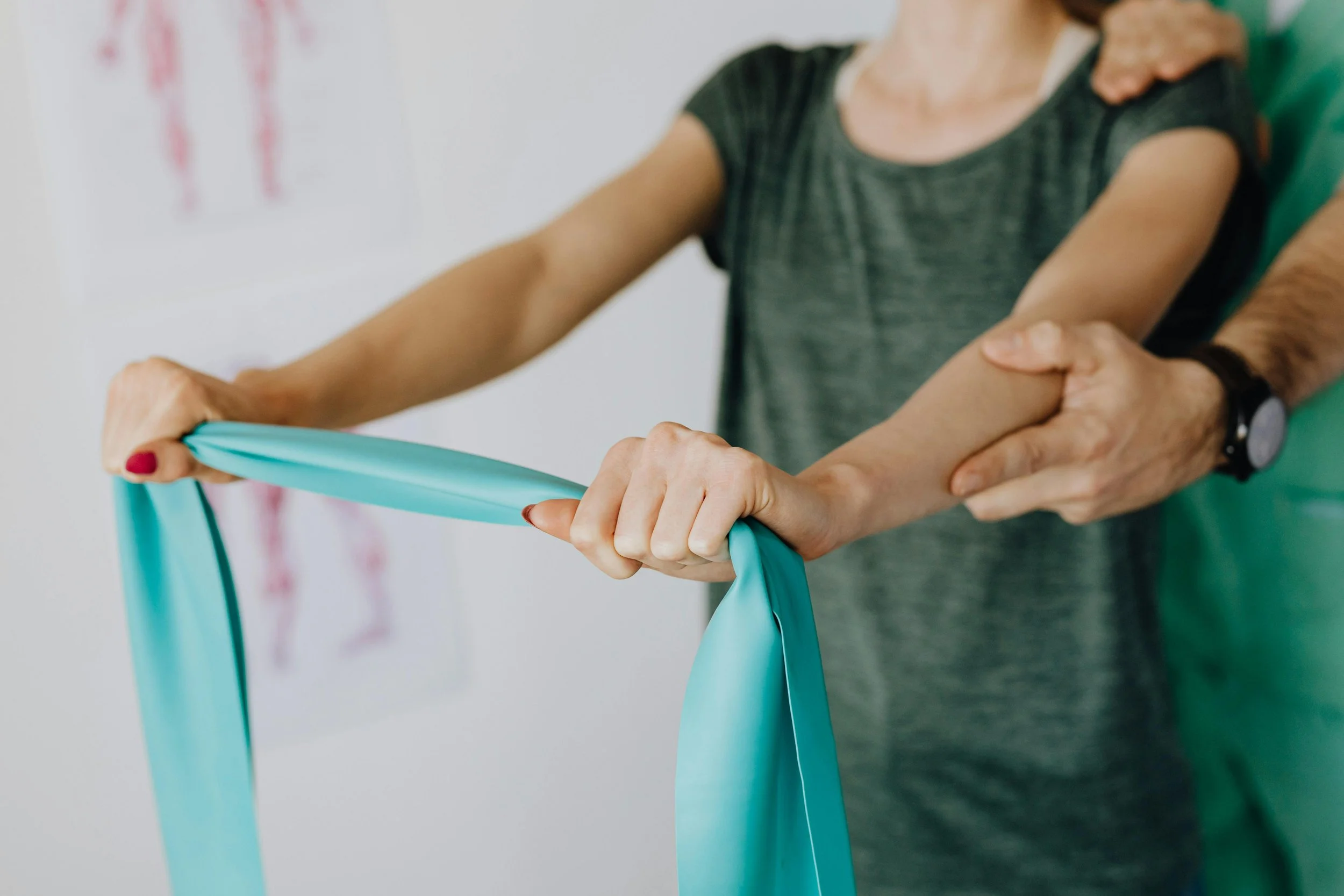 A woman doing physical therapy exercises with assistance from a therapist, using a resistance band.