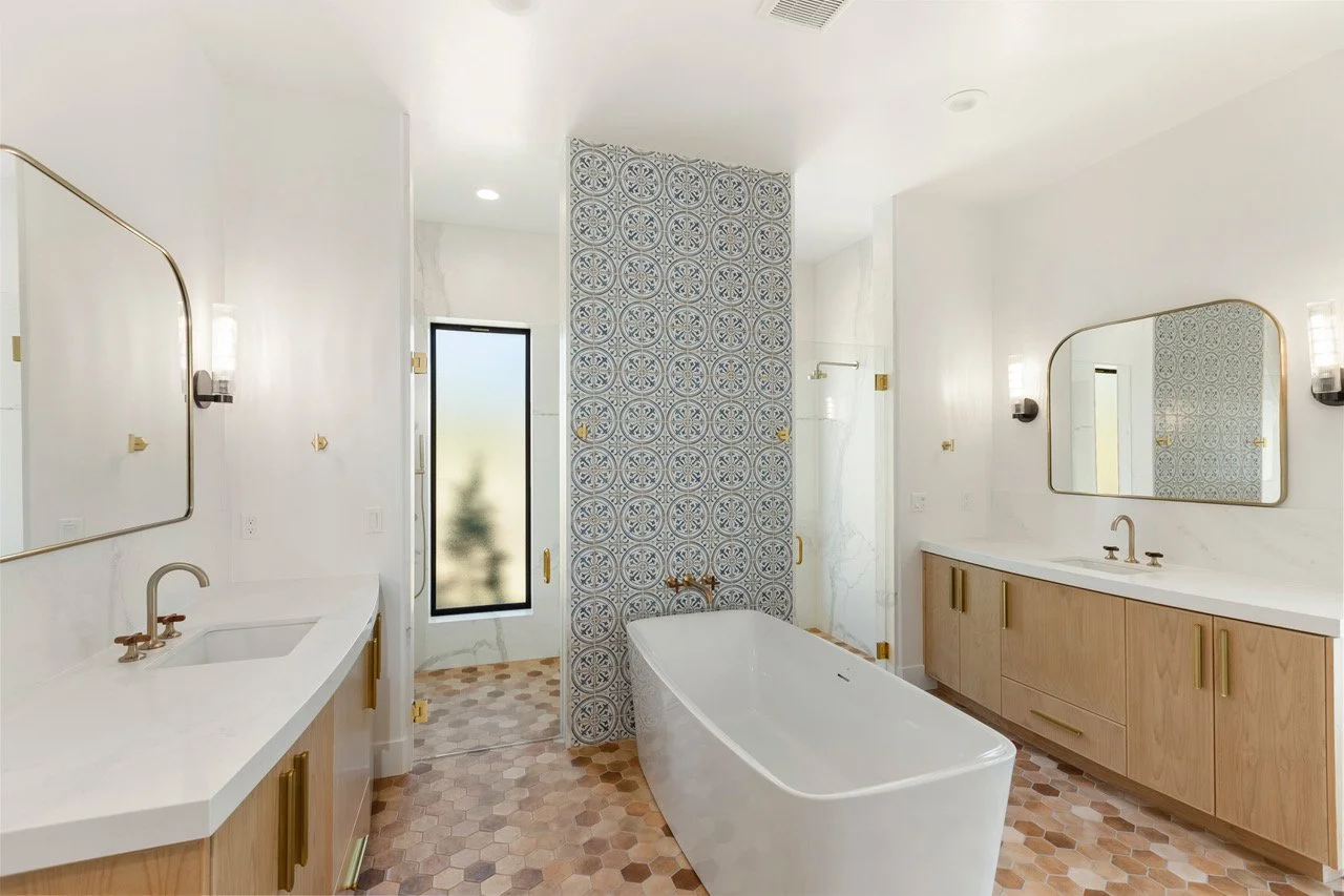 Modern bathroom with white walls, wooden cabinetry, a white bathtub, a large mirror, and patterned tile accents.
