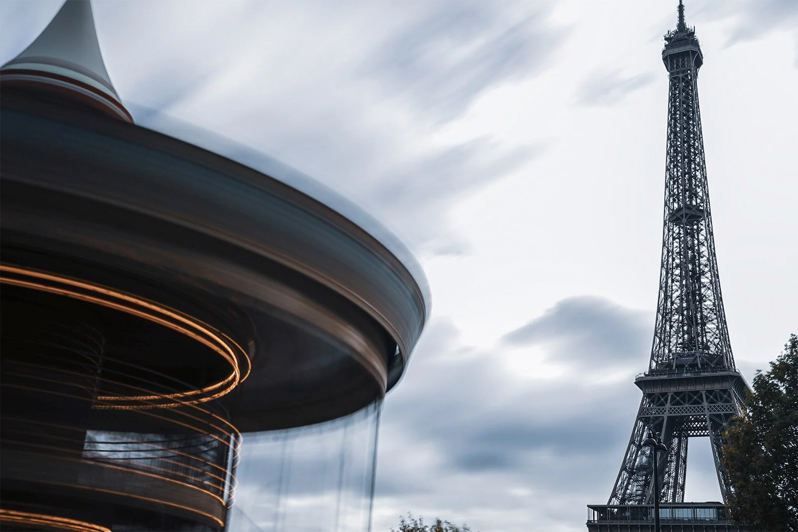 The Eiffel Tower in Paris with a modern building with illuminated spiral and horizontal lines in the foreground, under a cloudy sky.