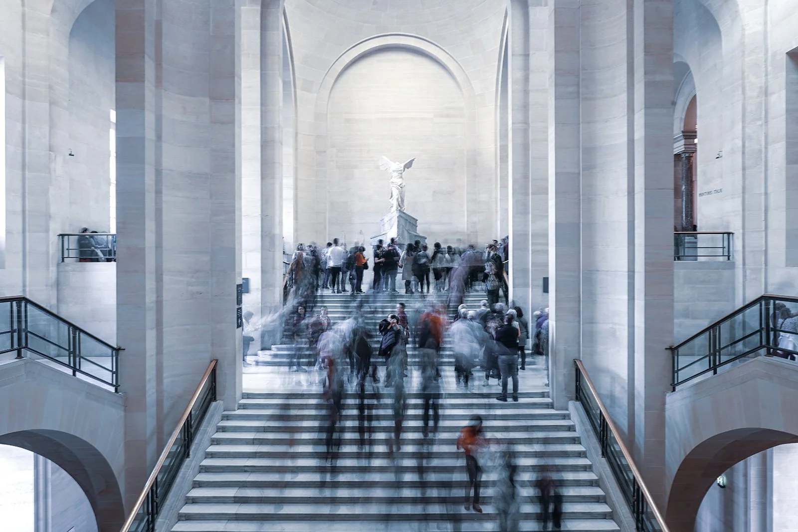 Inside the Lincoln Memorial with a marble interior, a large staircase leading to a memorial statue, and many visitors walking up and down the stairs, some blurred due to motion.