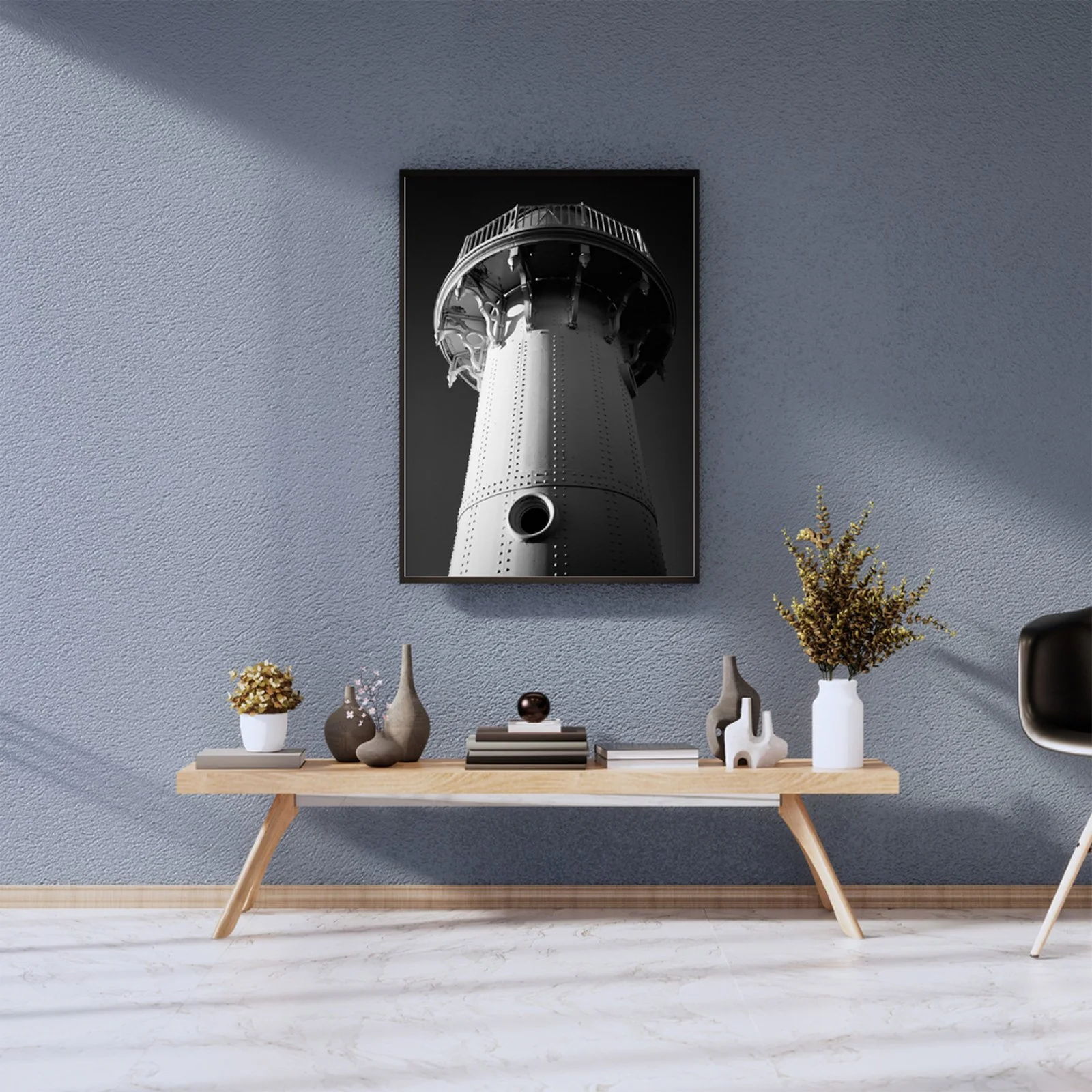 Black and white photo of a lighthouse on the wall in a modern living room, with a wooden table below decorated with vases, books, and a plant.